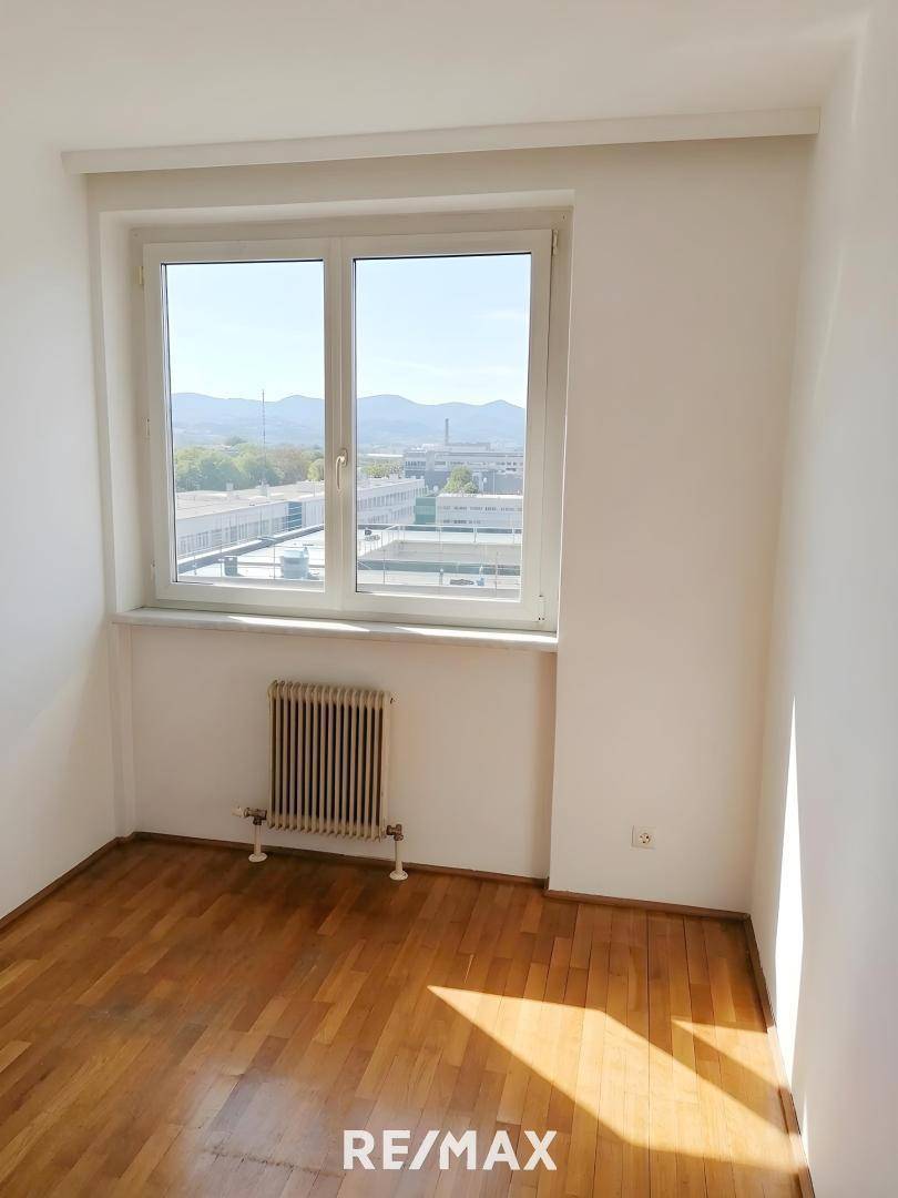 Lichtdurchfluteter Raum mit Parkettboden und einem Fenster mit weitem Blick auf die grüne Umgebung.