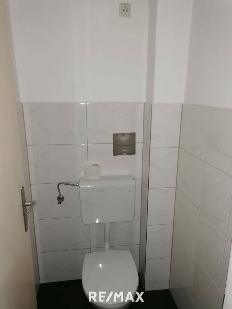Separates WC mit weißen Wandfliesen und einem einfachen, bodenstehenden Toilettenbecken.