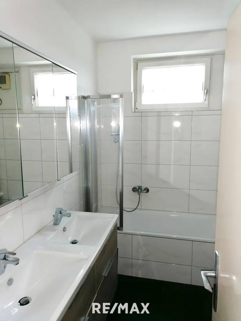 Modernes Badezimmer mit Doppelwaschbecken, Badewanne und Duschkabine, gut beleuchtet durch das Fenster.
