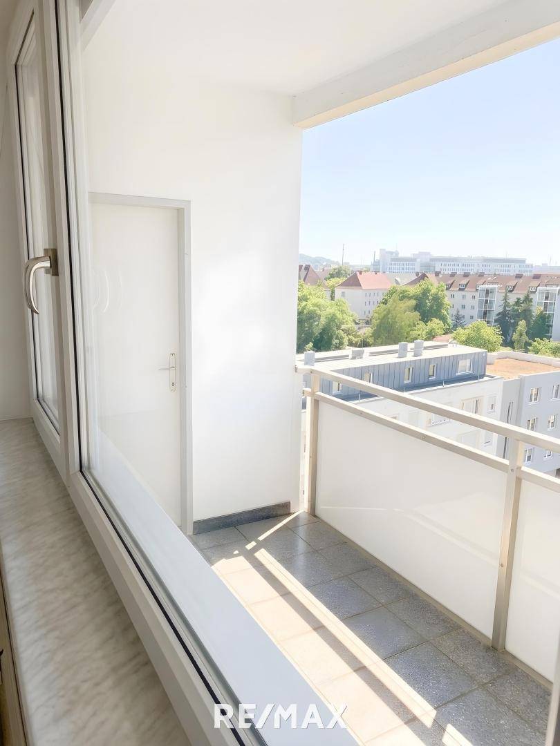Heller Balkon mit Fliesenboden und einem weiten Blick über die Stadt und die grüne Umgebung.