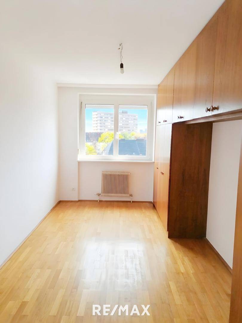 Schlafzimmer mit integrierten Holzschränken und Parkettboden, hell durch das große Fenster.