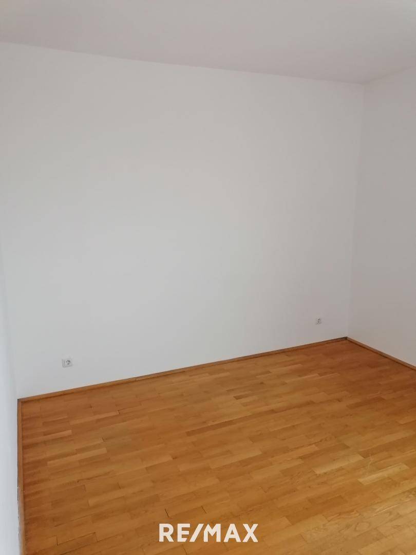 Leerer Raum mit weißen Wänden und einem gepflegten Parkettboden, ohne spezifische Merkmale.