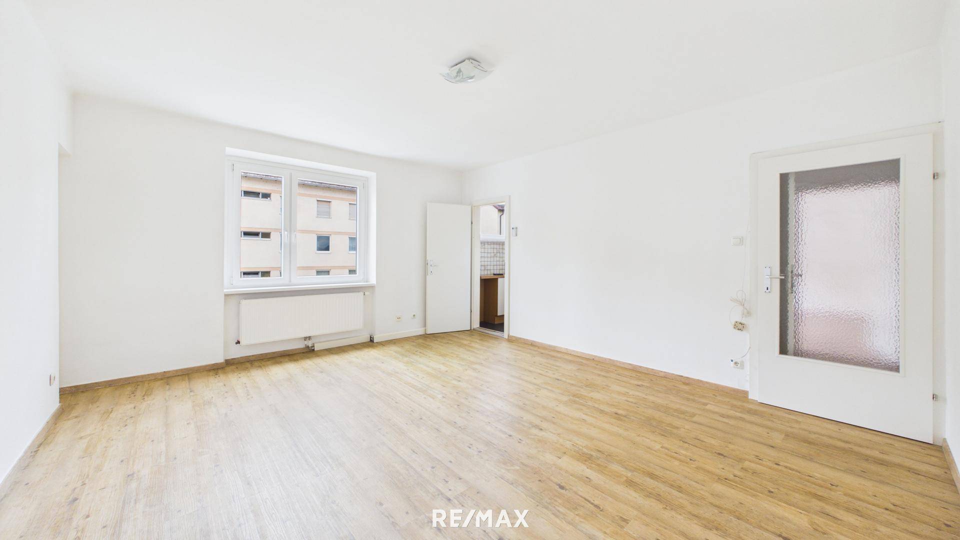 Geräumiges Zimmer mit Laminatboden und weißen Wänden, bietet Zugang zu einem weiteren Raum.