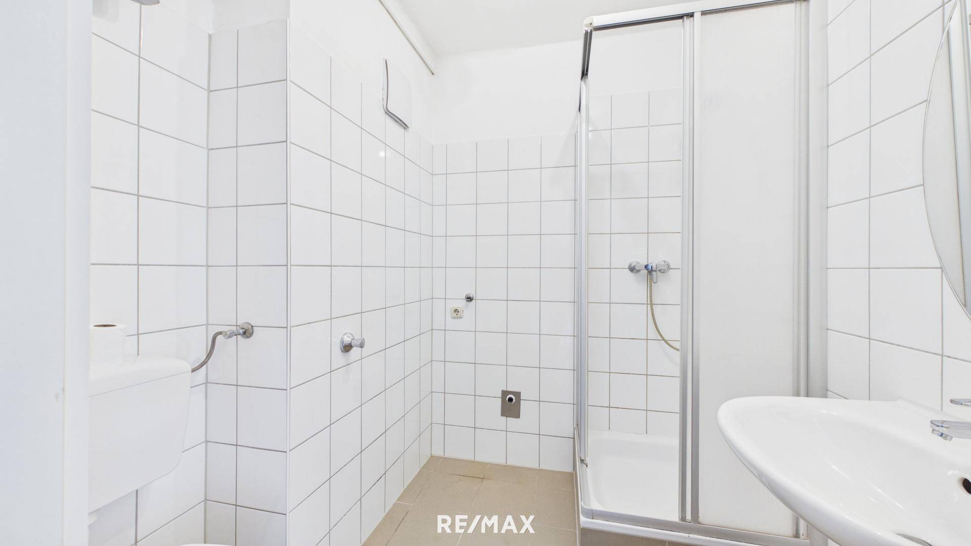 Gefliestes Badezimmer mit Dusche, WC und Waschbecken in schlichtem, funktionalem Design.