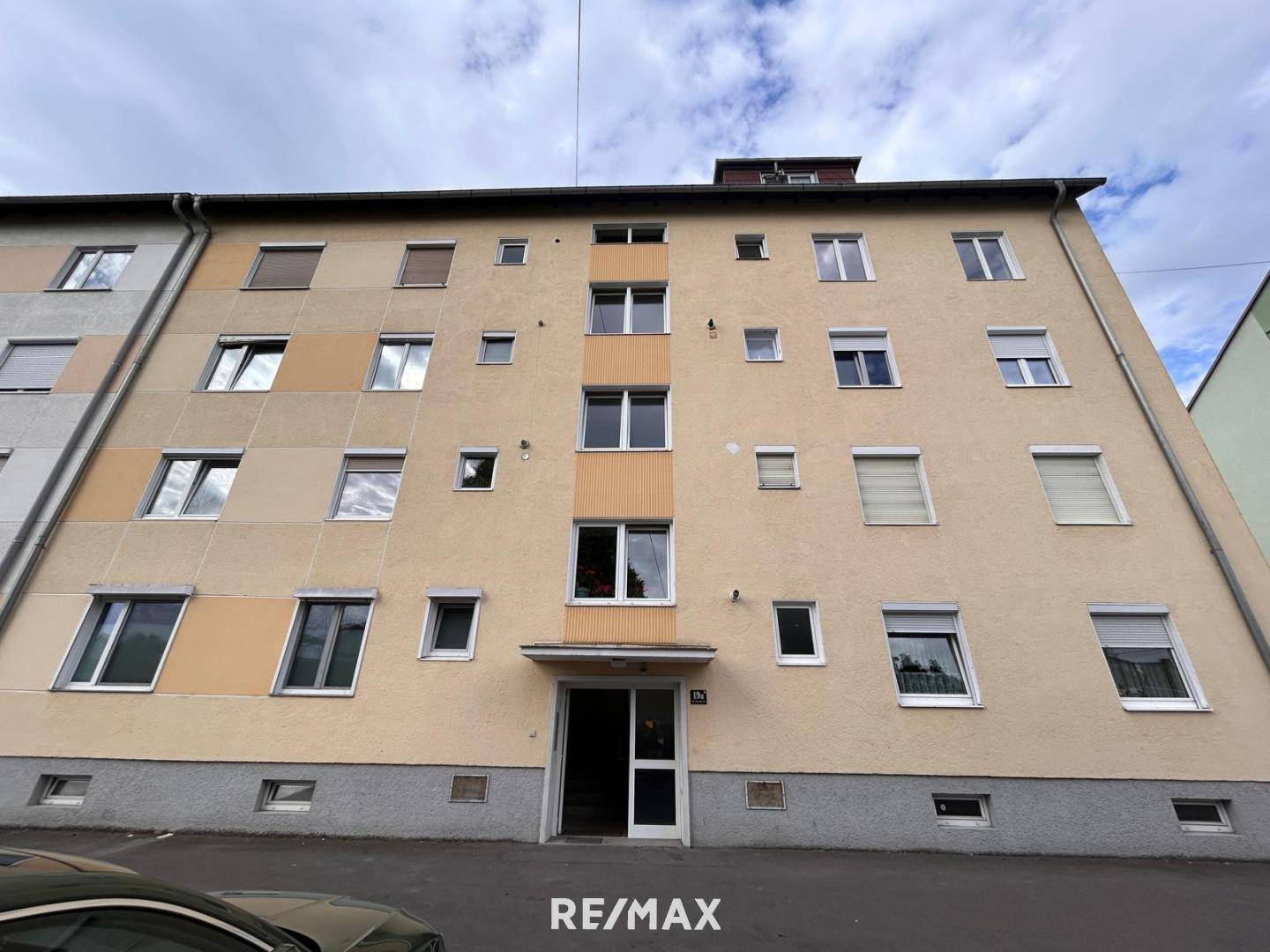 Mehrstöckiges Wohngebäude mit beiger Fassade und zahlreichen Fenstern unter bewölktem Himmel.