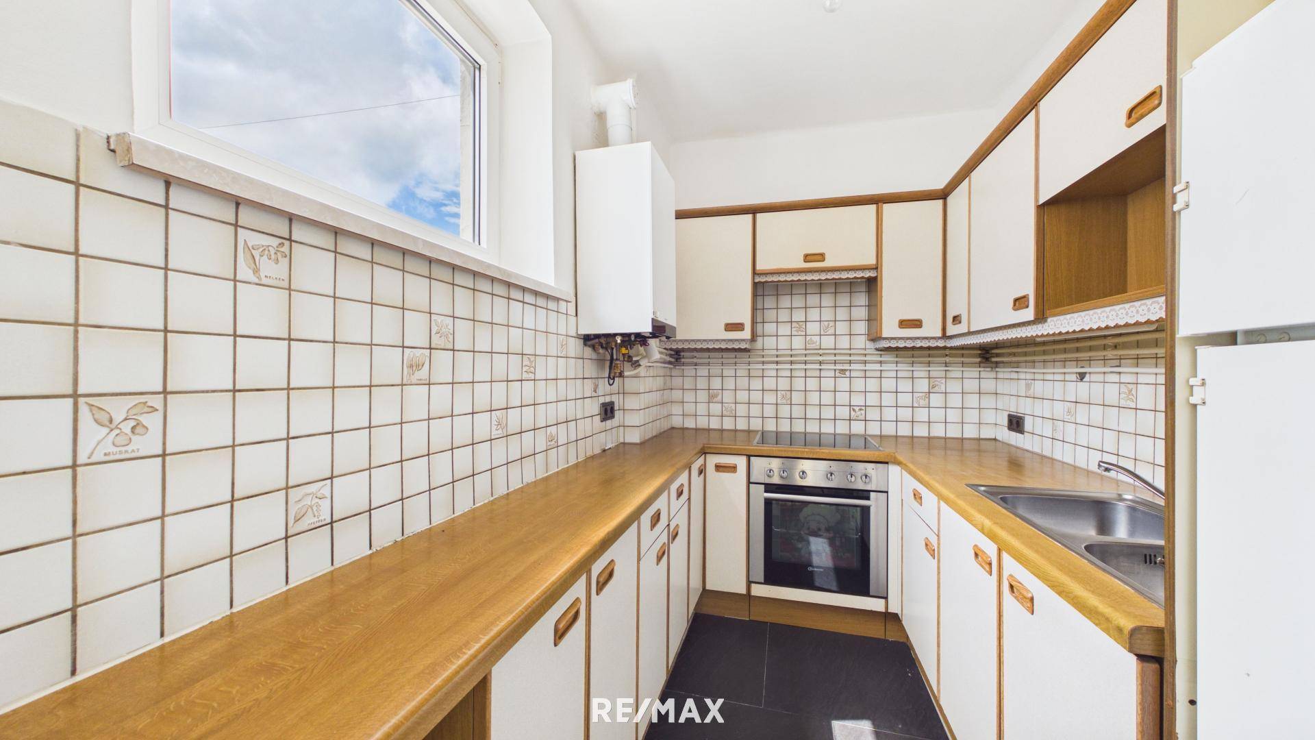 Funktionale Küche mit weißen Fliesen, Holz-Arbeitsplatten und integrierten Geräten sowie Fenster.