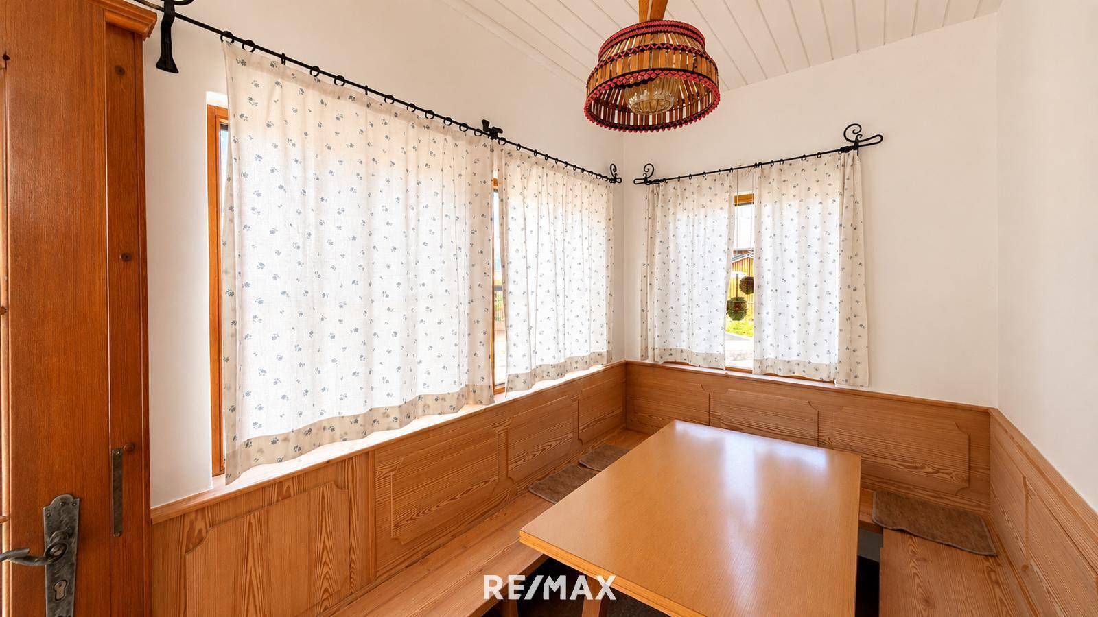 Gemütlicher Essbereich mit Holzbänken, Holztisch und traditionellen Vorhängen, hell durch Fenster.