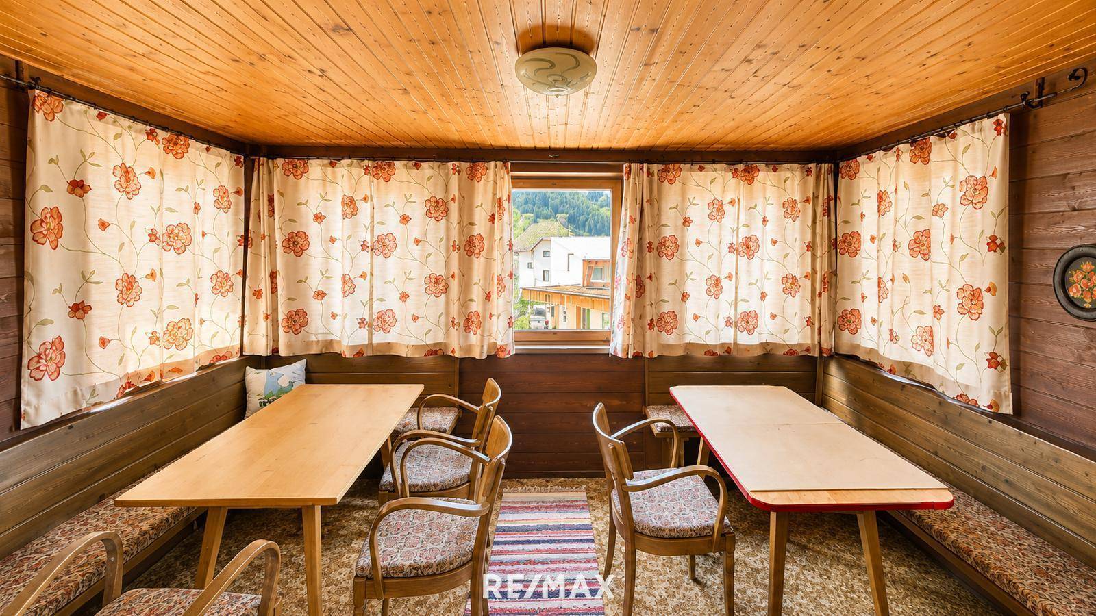 Rustikaler Essbereich mit Holztäfelung, Holztischen und floralen Vorhängen, gemütlich und traditionell.