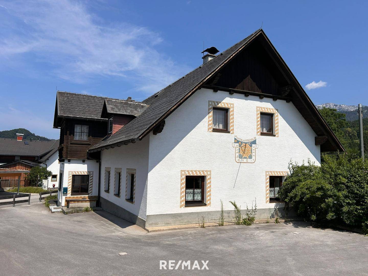 Charmantes Landhaus mit traditioneller Fassadenmalerei und Bergblick unter strahlend blauem Himmel.
