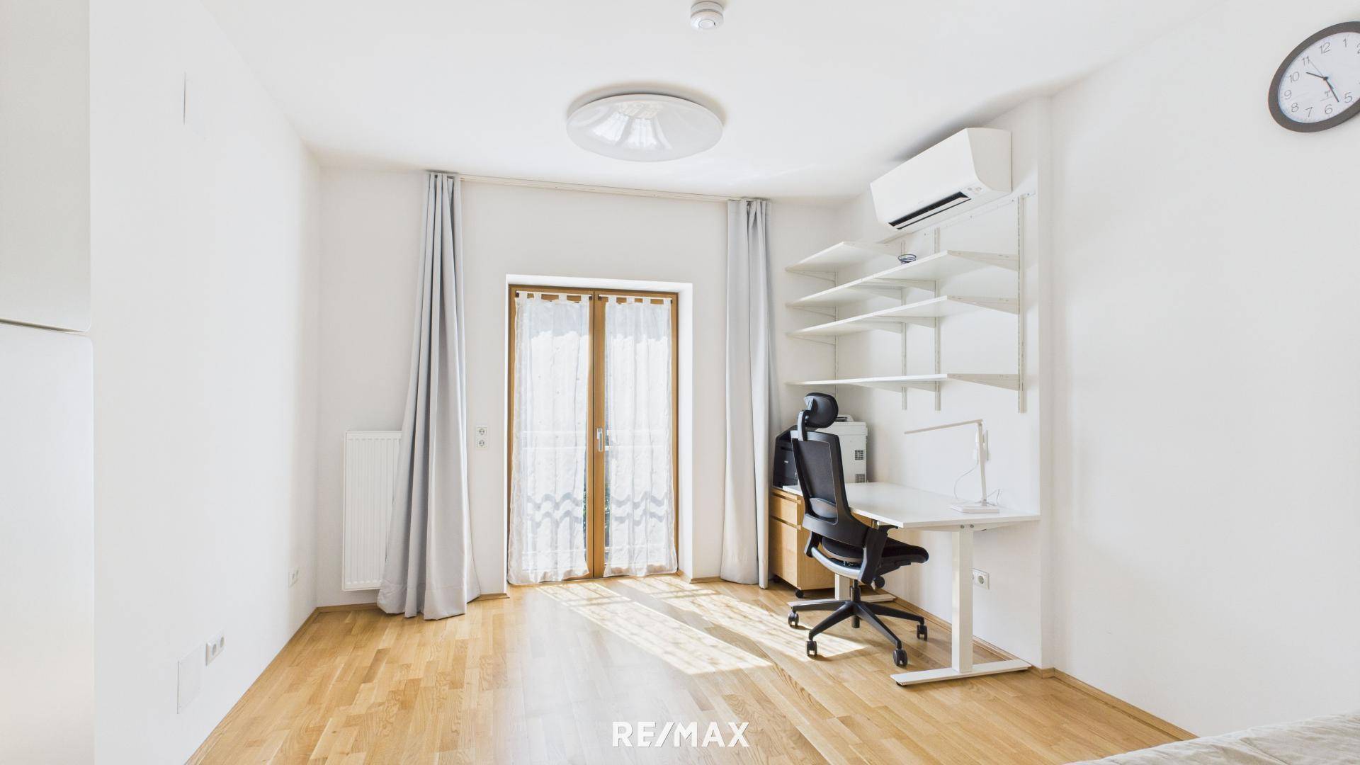 Helles Arbeitszimmer mit Holzboden, Schreibtisch und Zugang zu einem Balkon oder Terrasse.