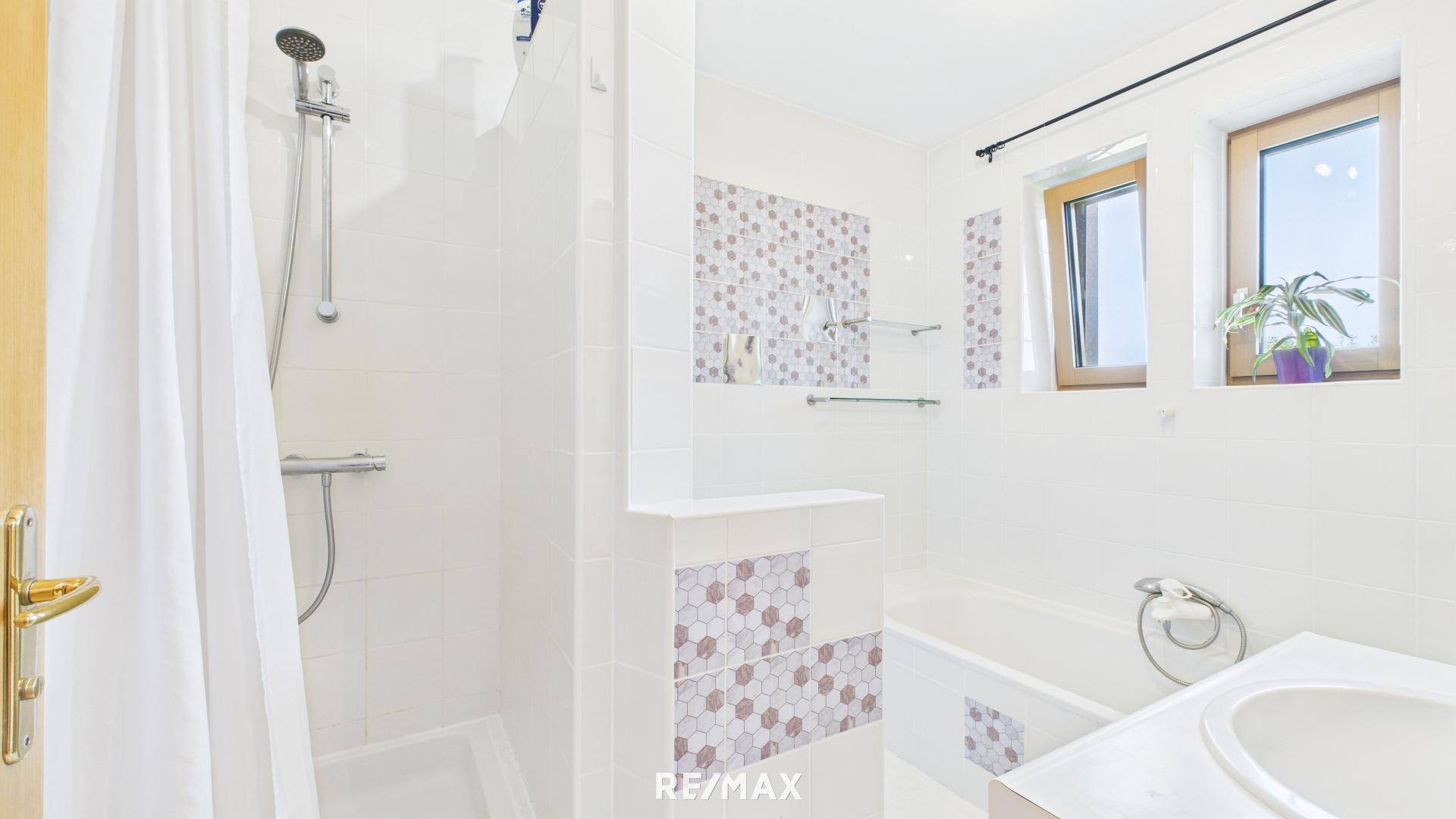 Modernes Badezimmer mit Dusche, Badewanne und Fenster, hell gefliest.