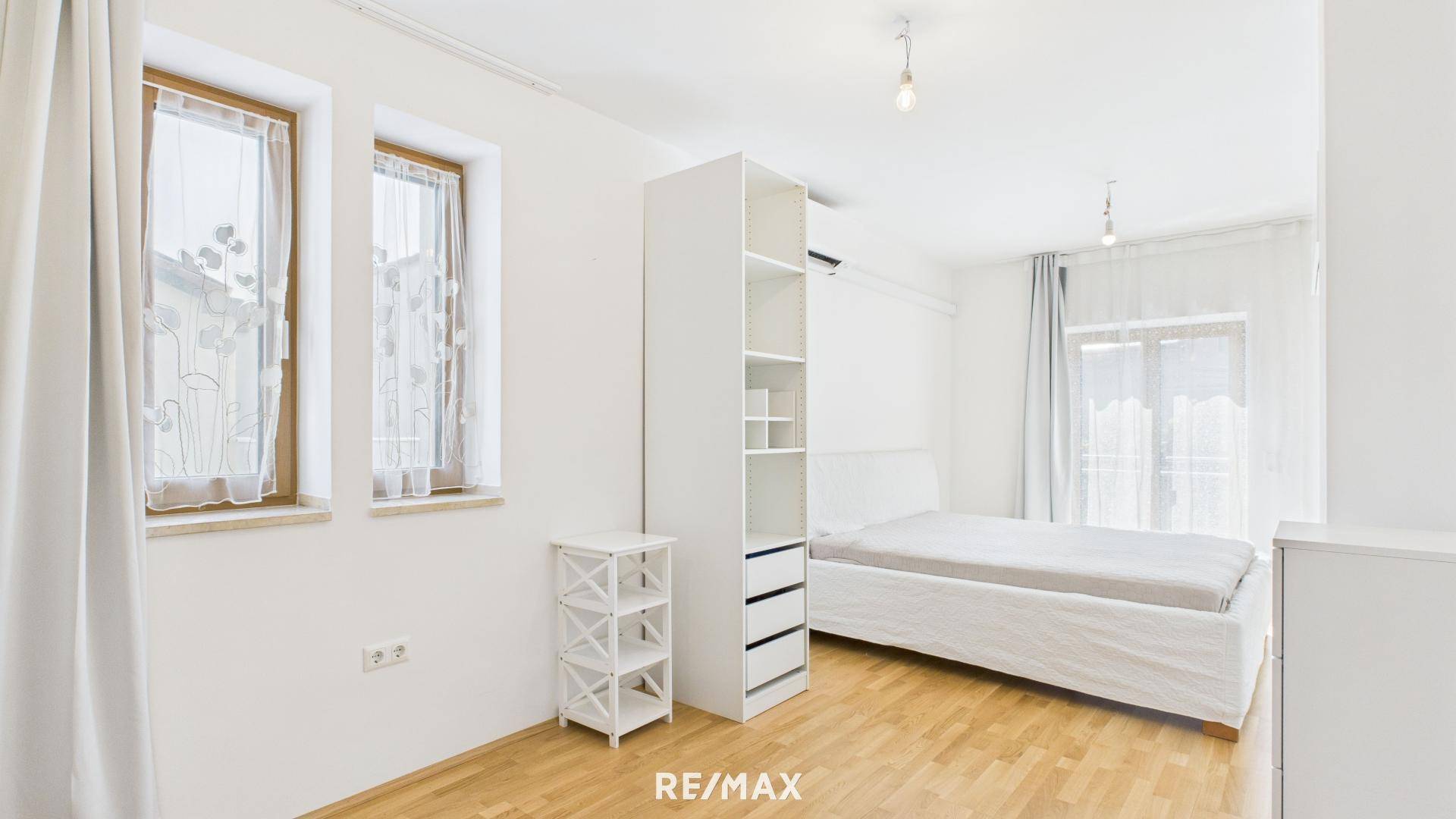 Schlafzimmer mit Holzboden, weißem Bett und Kleiderschrank, hell und geräumig.