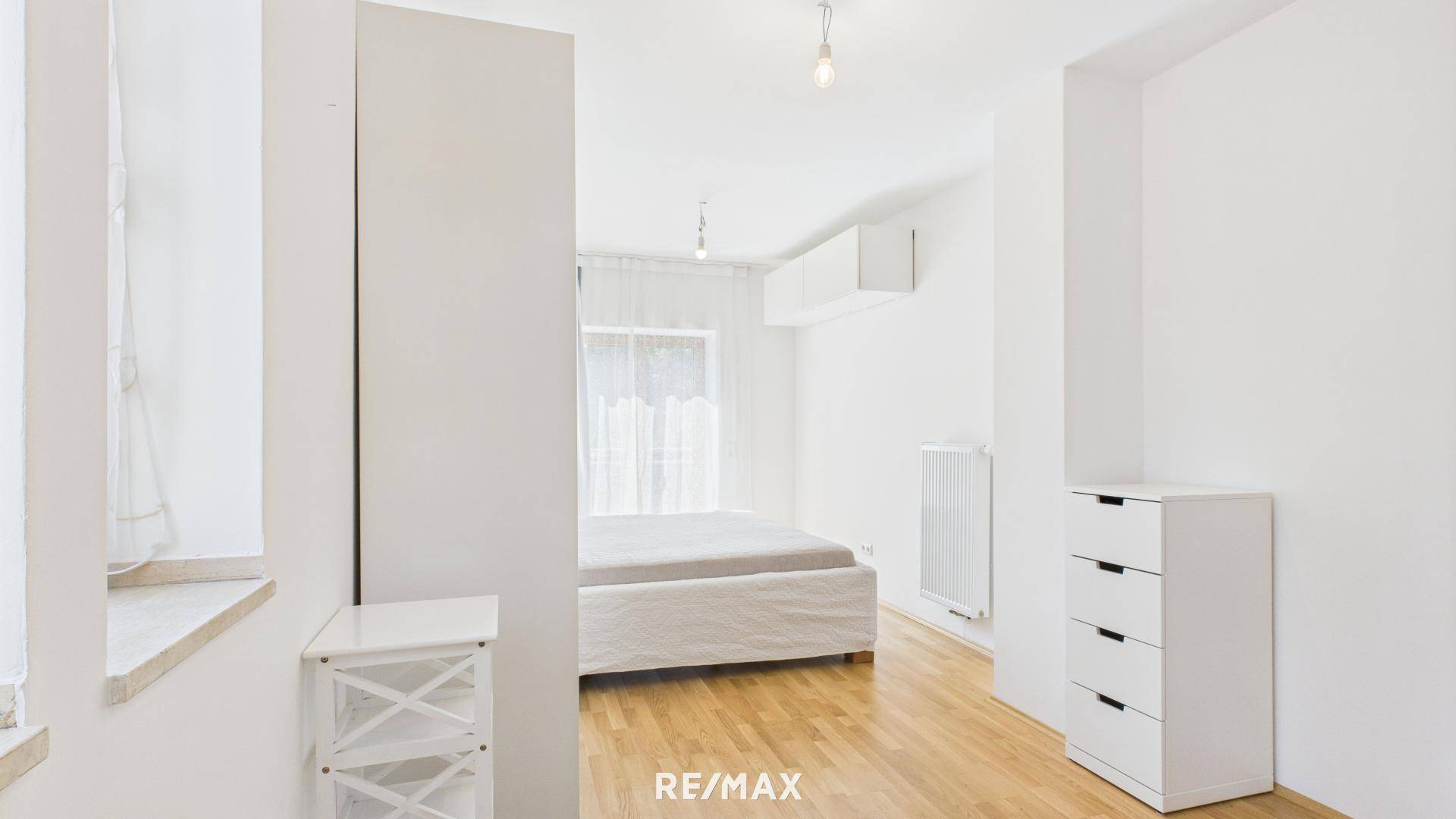 Helles Schlafzimmer mit Holzboden, weißem Bett und Kommode, bietet viel Platz.