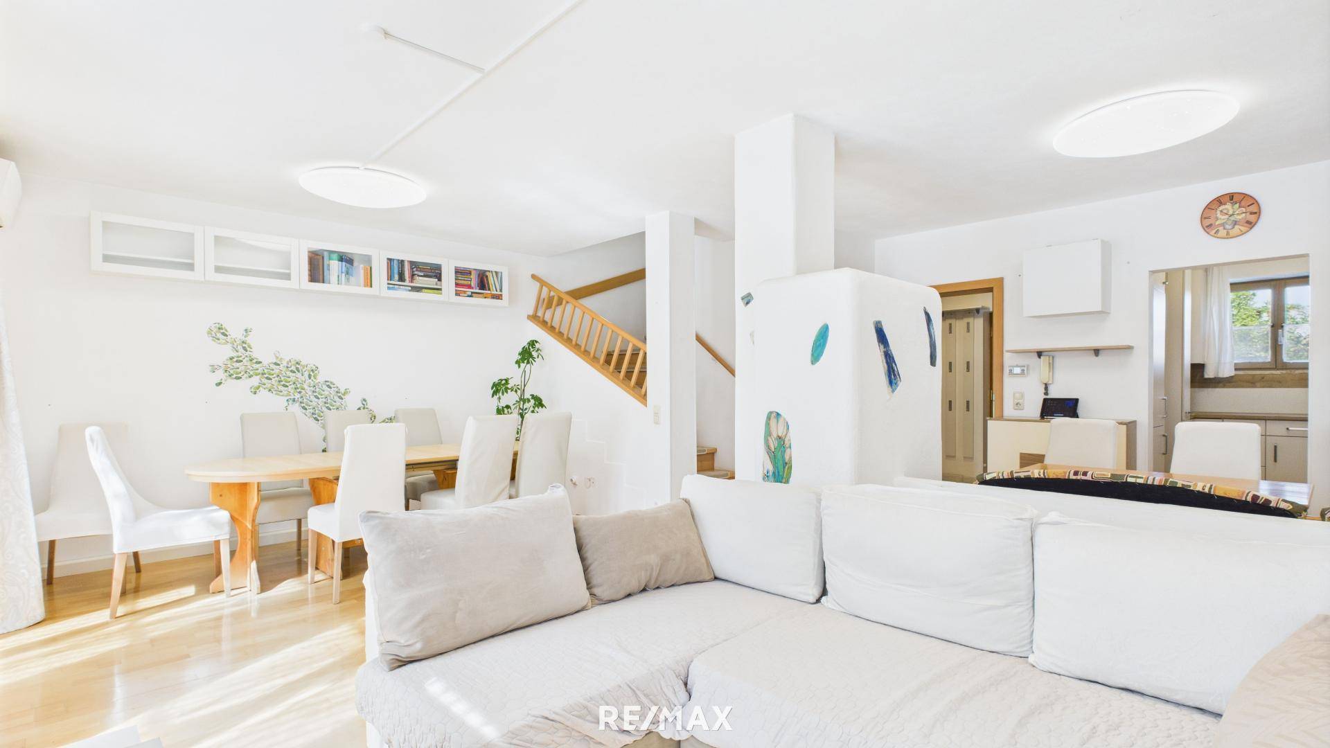 Geräumiger Wohn-Essbereich mit hellem Sofa, Esstisch und Treppenaufgang.