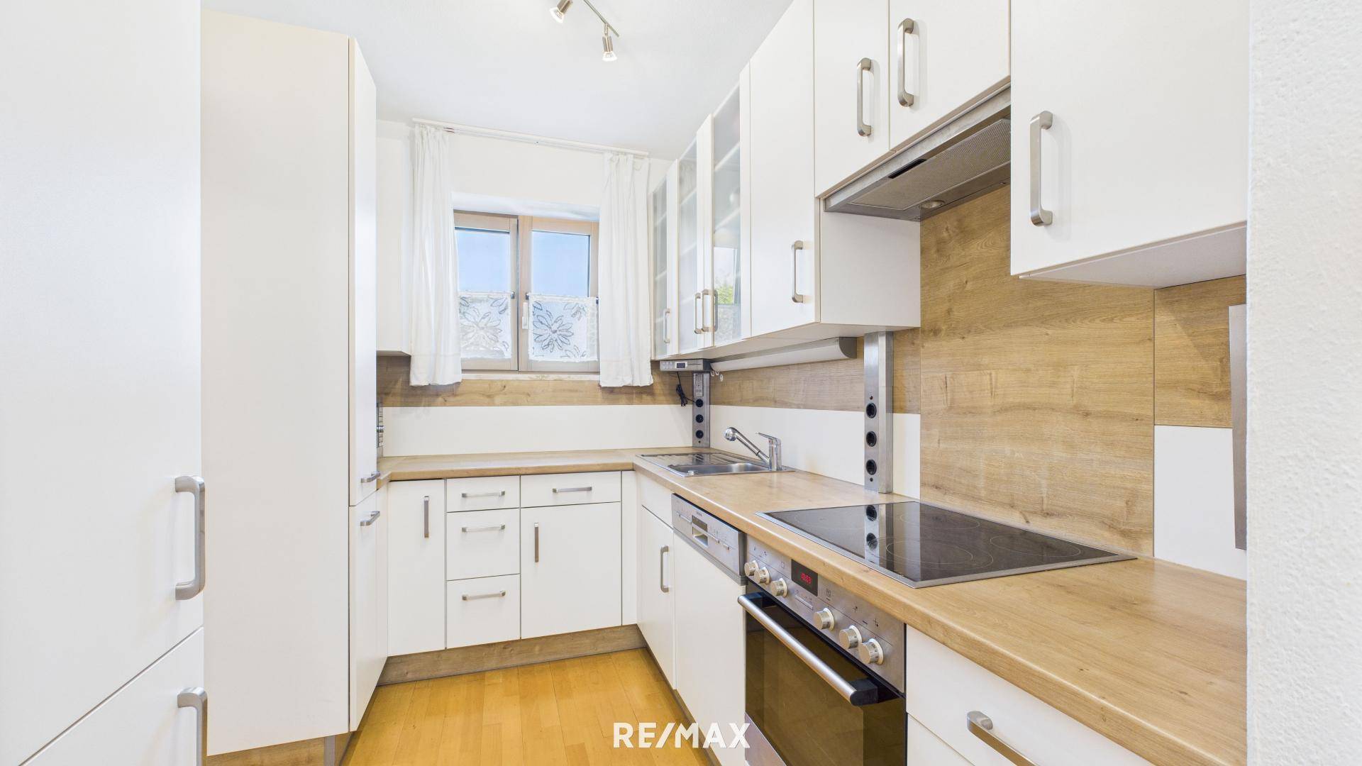 Helle Küche mit weißen Schränken, Holzoptik-Arbeitsplatte und modernen Geräten.