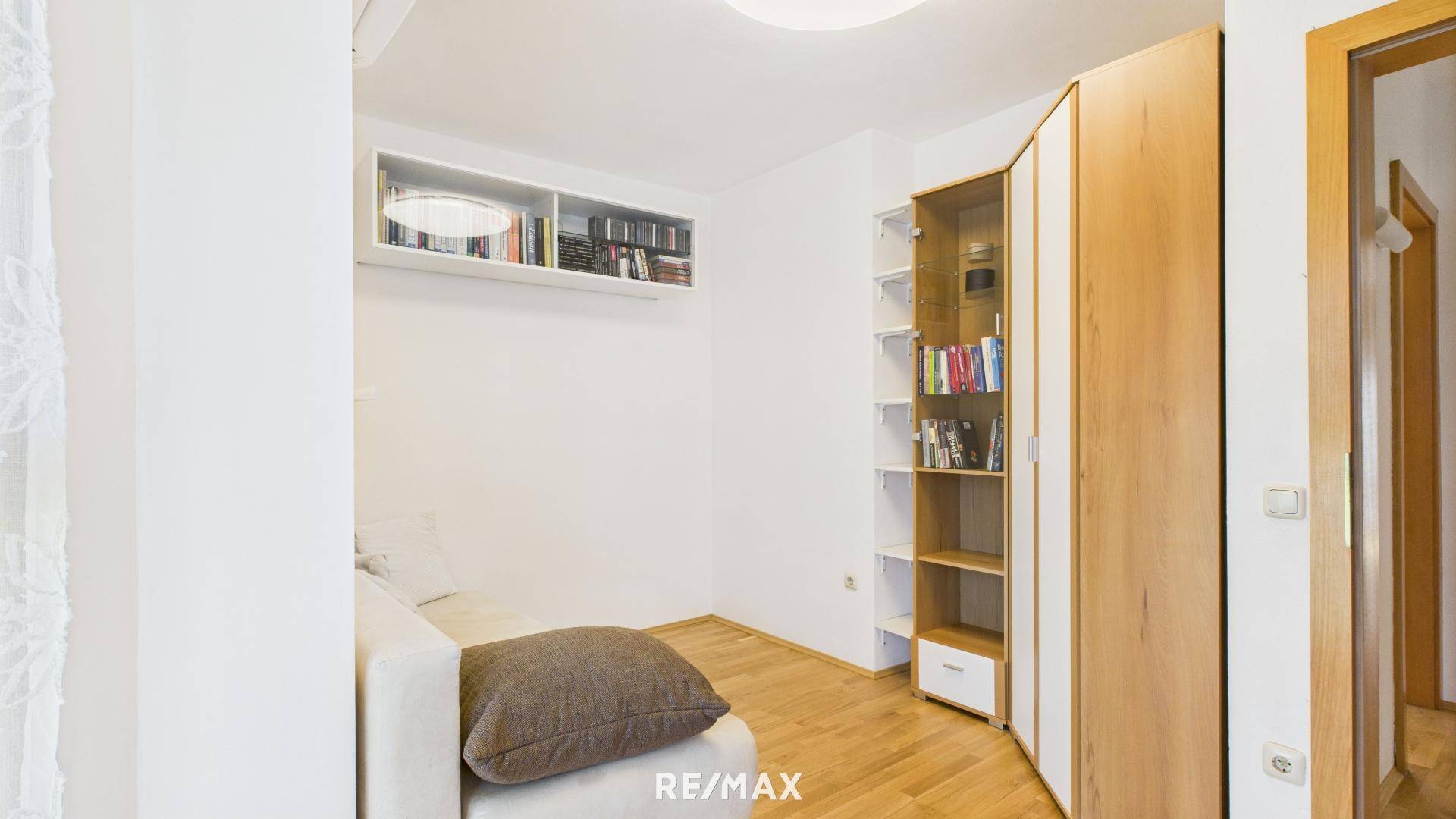 Kleines Zimmer mit Sofa, Bücherregal und Holzboden, ideal als Arbeits- oder Gästezimmer.