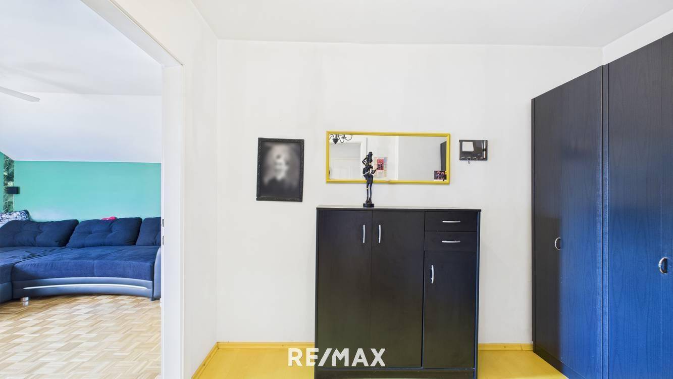 Eingangsbereich mit schwarzem Schrank, blauer Garderobe und gelbem Boden, mit Blick ins Wohnzimmer.