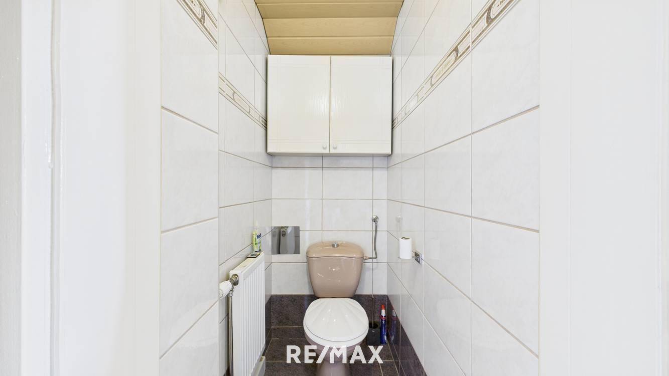 Kleines WC mit weißen Fliesen, beiger Toilette und Heizkörper.