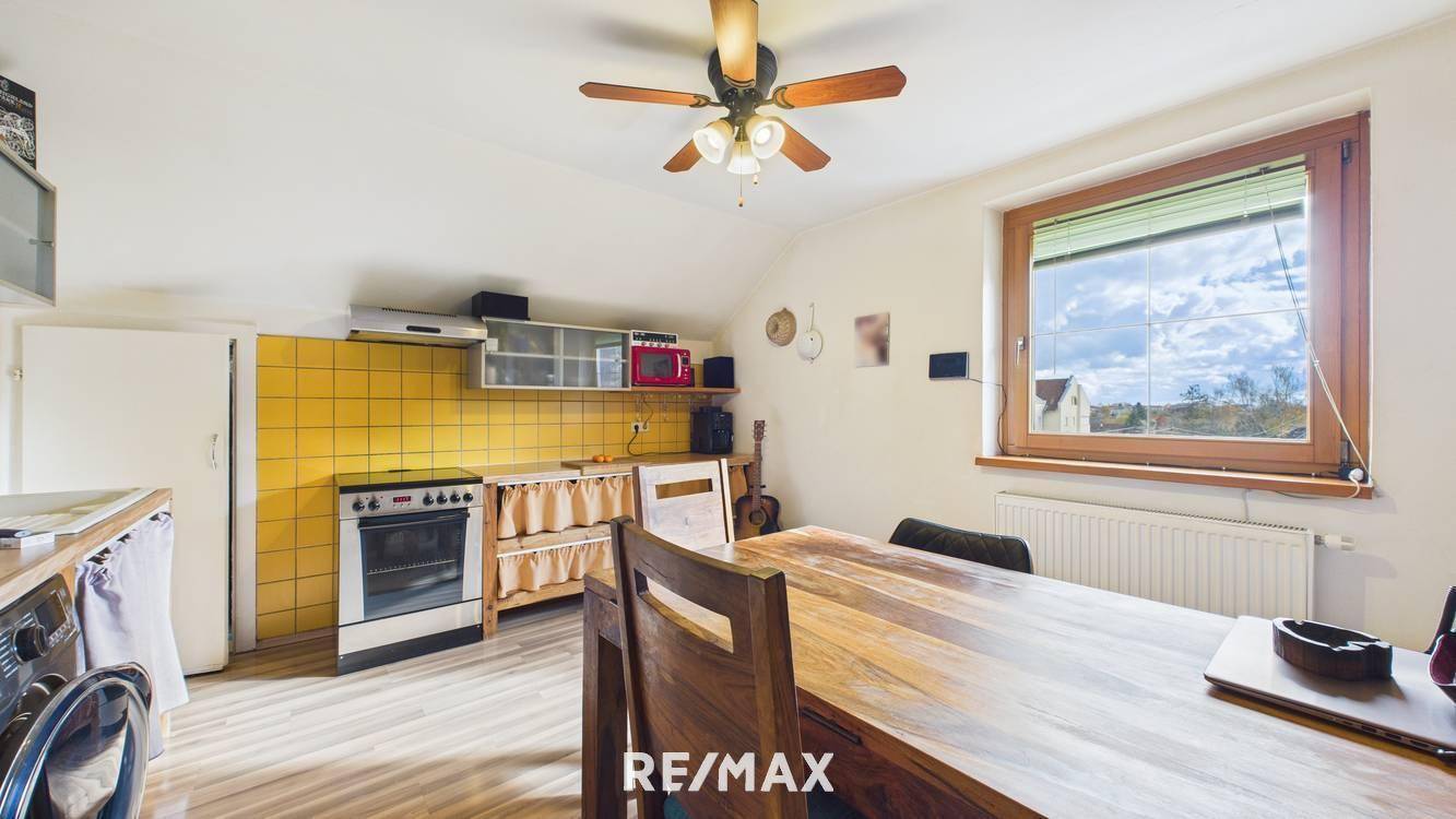 Wohnküche mit Holztisch, gelbem Fliesenspiegel und Deckenventilator, hell durch großes Fenster.