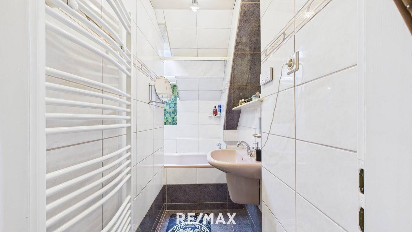 Helles Badezimmer mit weißen Fliesen, Badewanne, Waschbecken und beheiztem Handtuchhalter unter der Dachschräge.