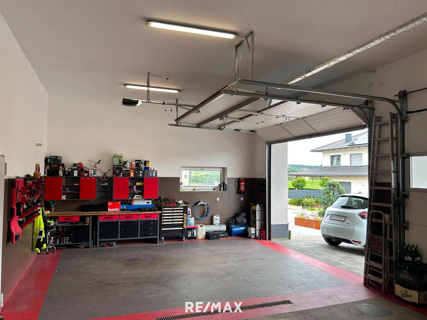 Offene Garage mit Blick nach draußen auf ein geparktes Auto und ein Wohnhaus im Hintergrund.