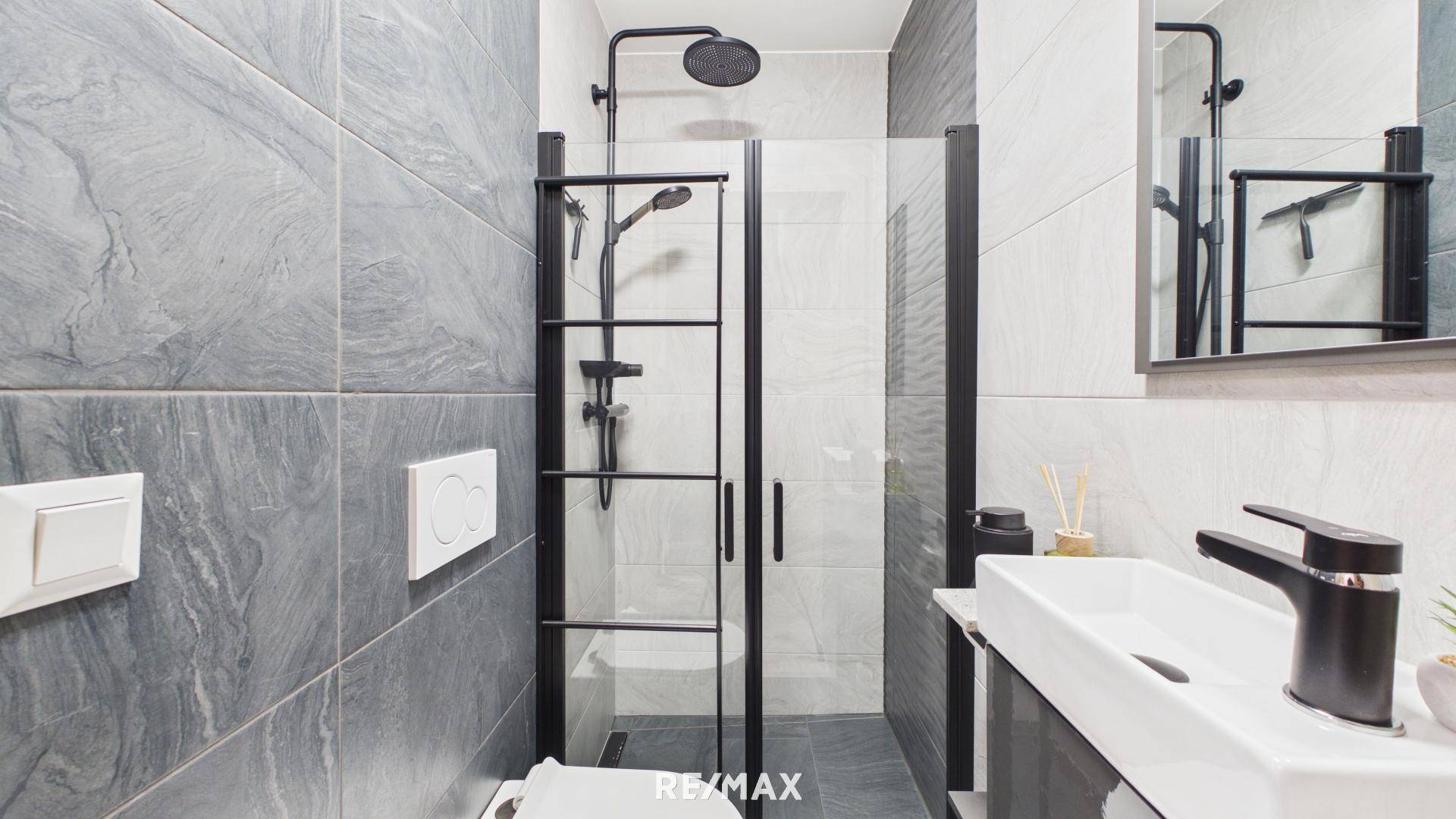 Modernes Badezimmer mit grauen Fliesen, Duschkabine und schwarzer Armatur.