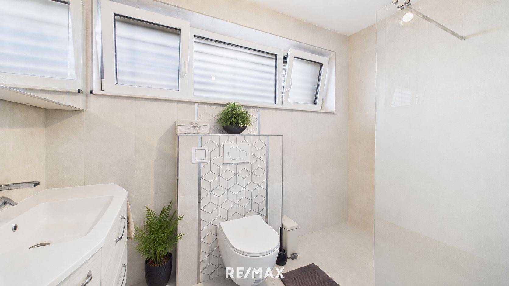 Modernes Badezimmer mit WC, Waschbecken, Duschbereich und Fenster, hell gefliest und funktional eingerichtet.