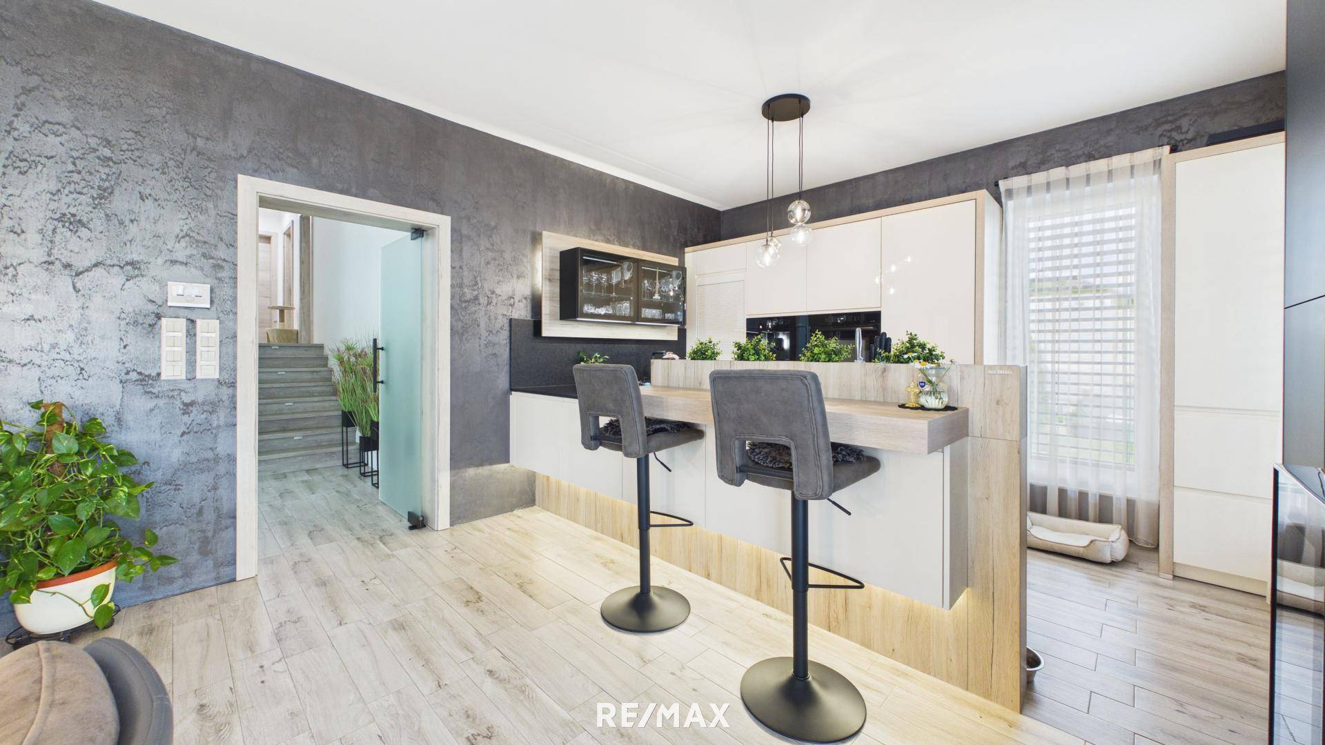 Moderne Küche mit Frühstücksbar, weißen Schränken und dunkler Arbeitsplatte.