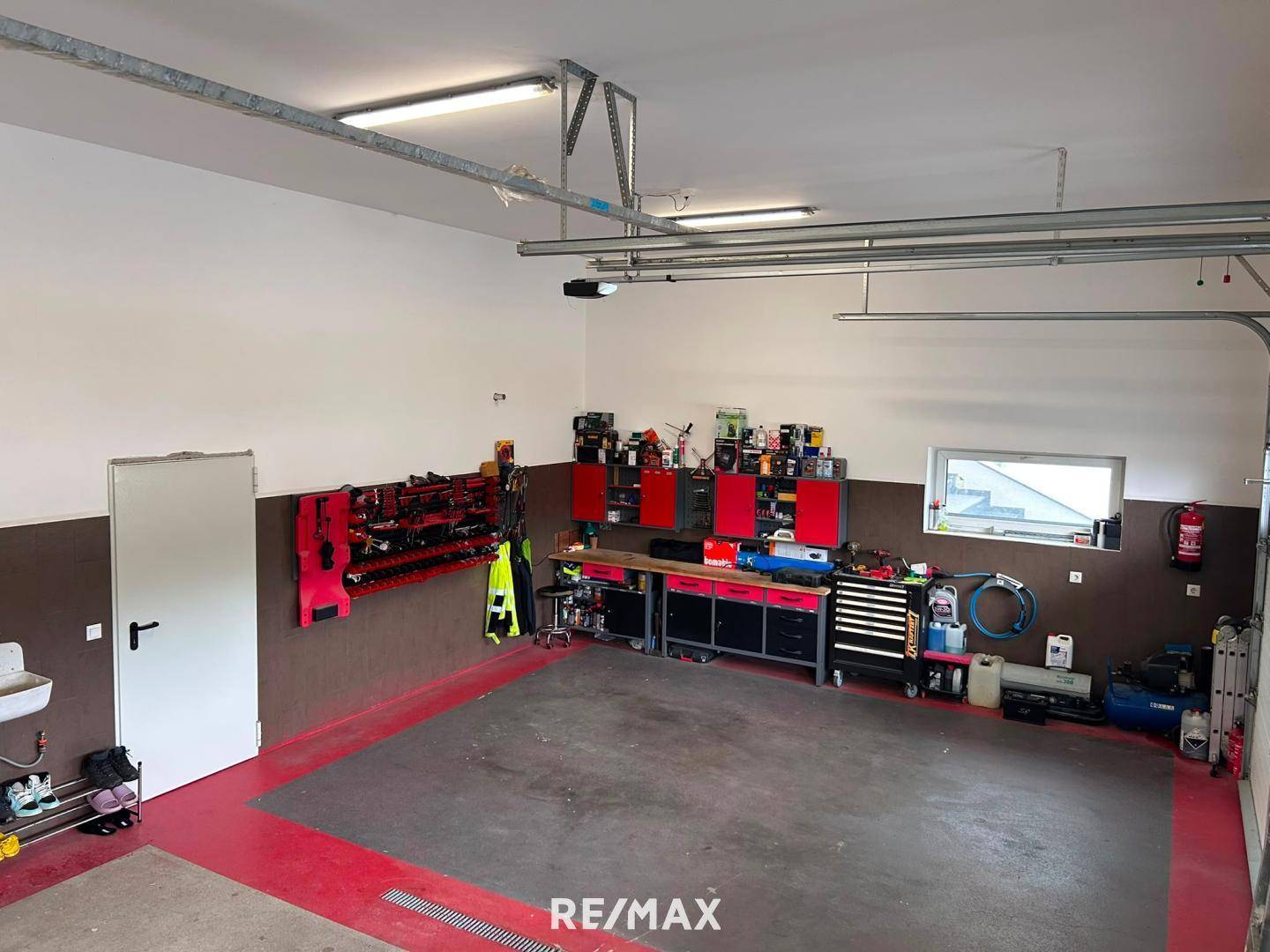 Übersicht über den Werkstattbereich der Garage mit roten Schränken, Werkzeugen und einem Fenster.