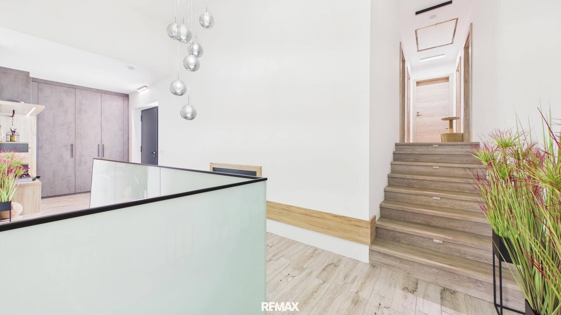 Heller Flur mit Holztreppe, Glasgeländer und moderner Deckenleuchte.