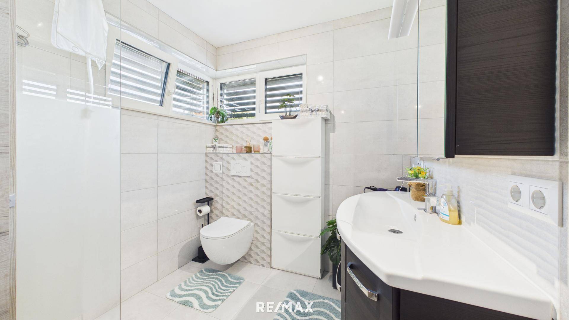 Modernes Badezimmer mit weißen Fliesen, wandhängendem WC und großer Dusche.