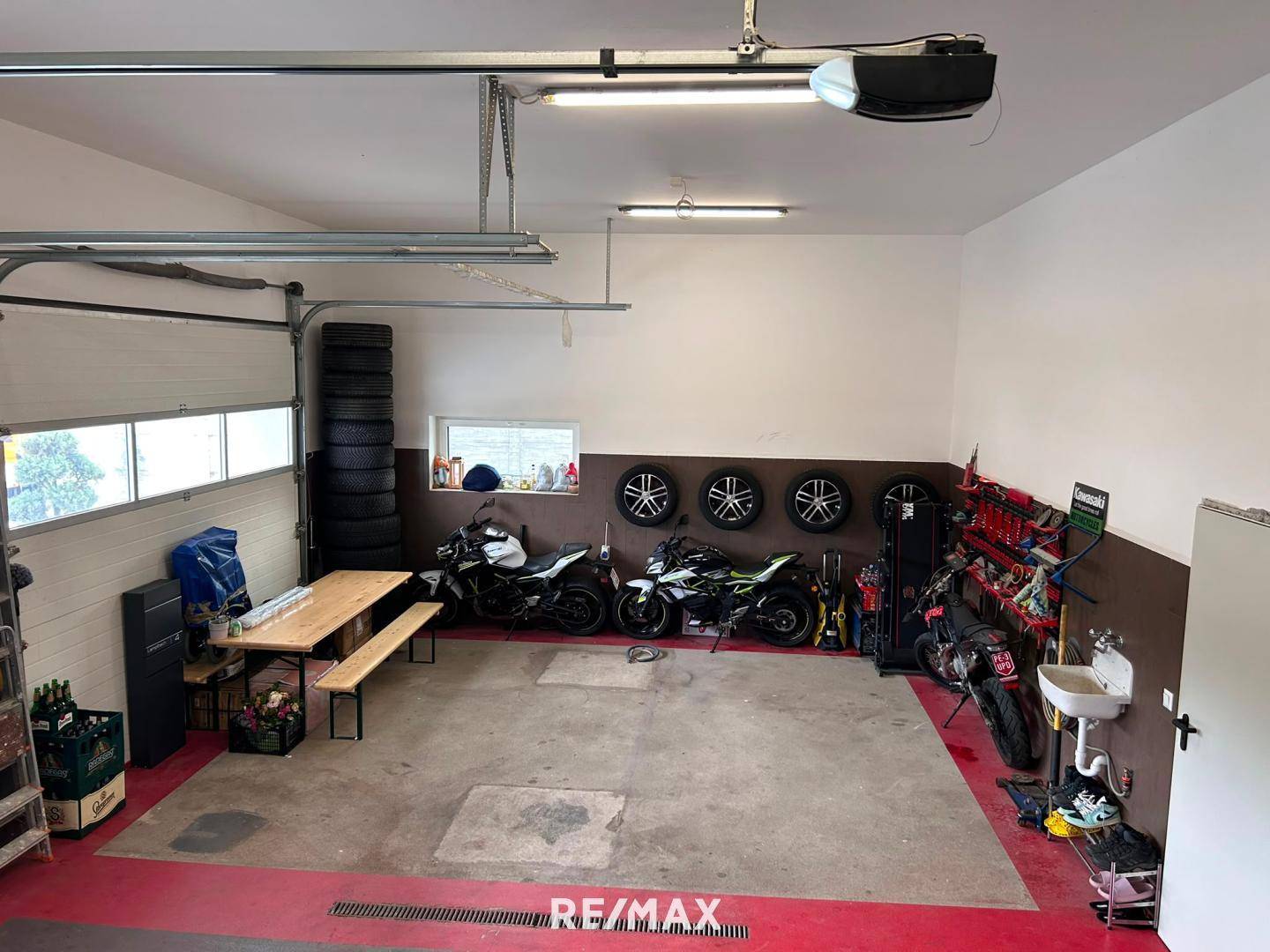 Geräumige Garage mit Motorrädern, Reifenstapeln, Werkbank und einem Biertisch für gesellige Runden.