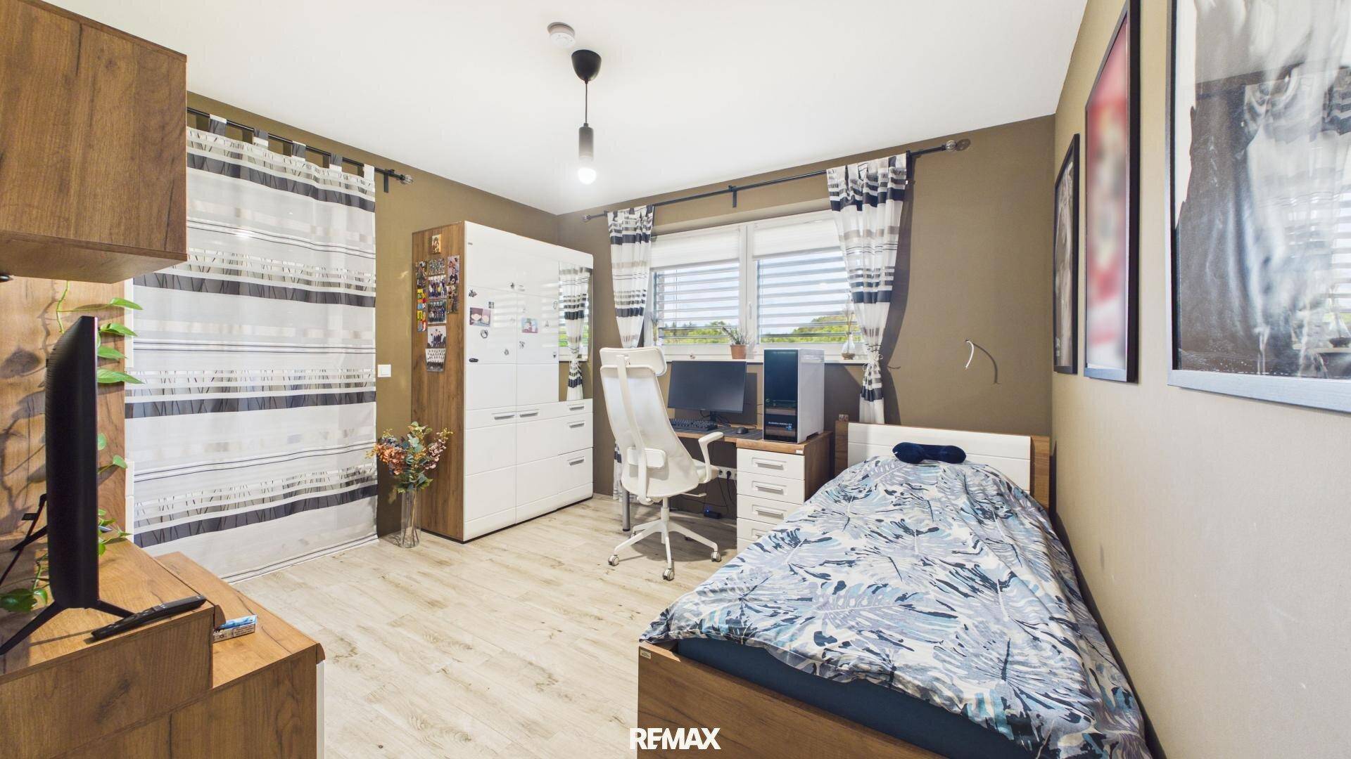 Schlafzimmer mit Einzelbett, Schreibtisch und Kleiderschrank in neutralen Farben.