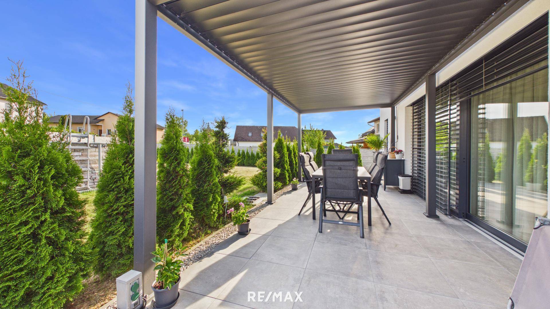Große überdachte Terrasse mit modernen Gartenmöbeln, Fliesenboden und Blick in den grünen Garten.
