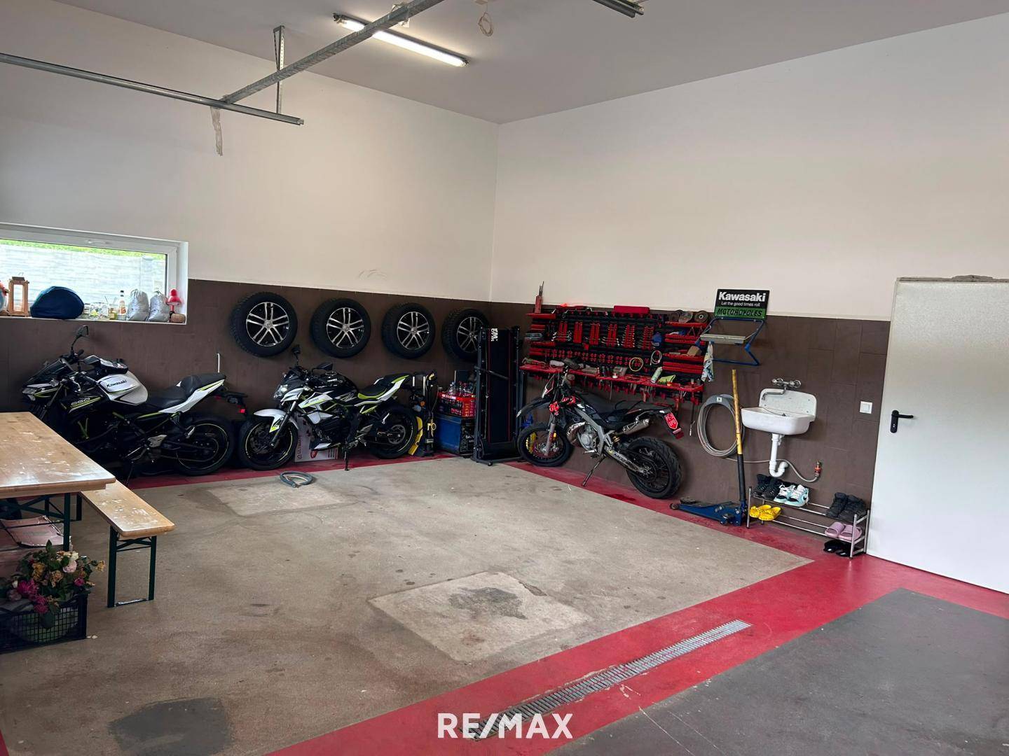 Geräumige Garage mit mehreren Motorrädern, Ersatzreifen und einem praktischen Waschbecken an der Wand.