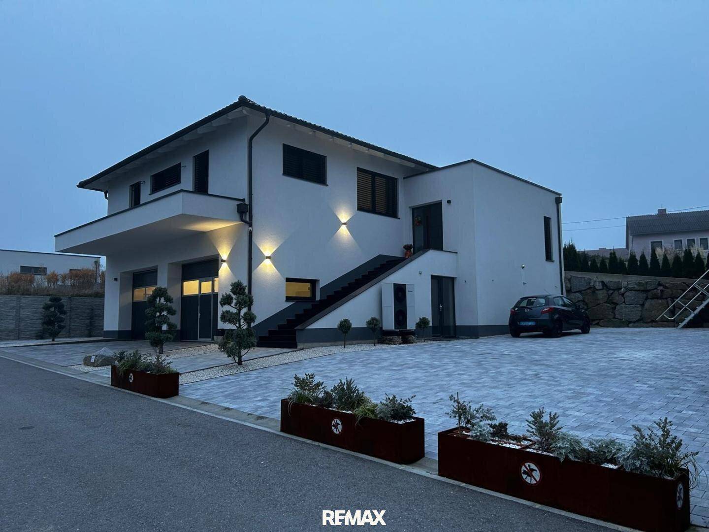 Modernes Haus bei Dämmerung mit beleuchteter Fassade und gepflegter Außenanlage.