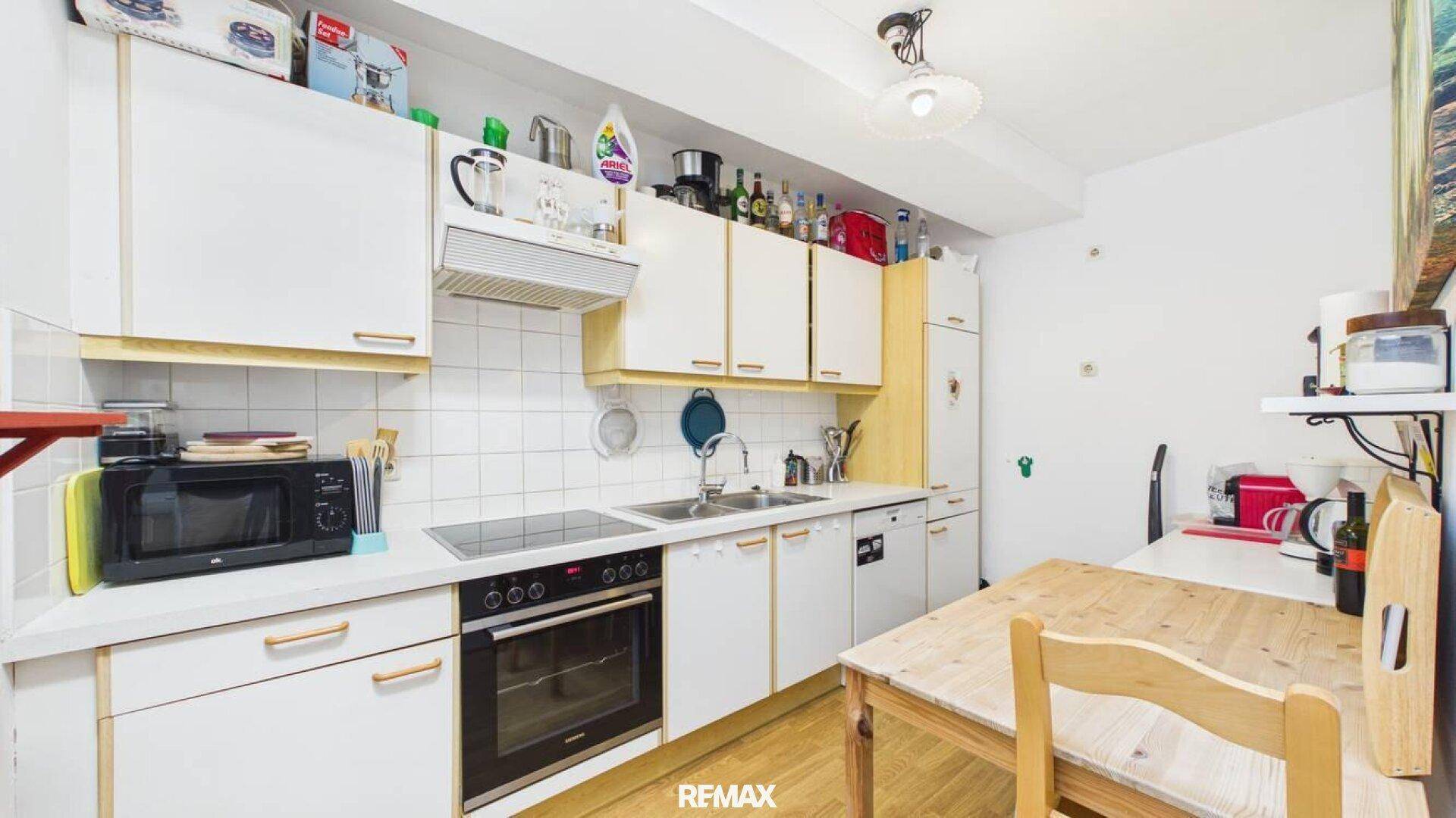 Funktionale Küche mit weißen Schränken, Fliesenrückwand und kleinem Essbereich.