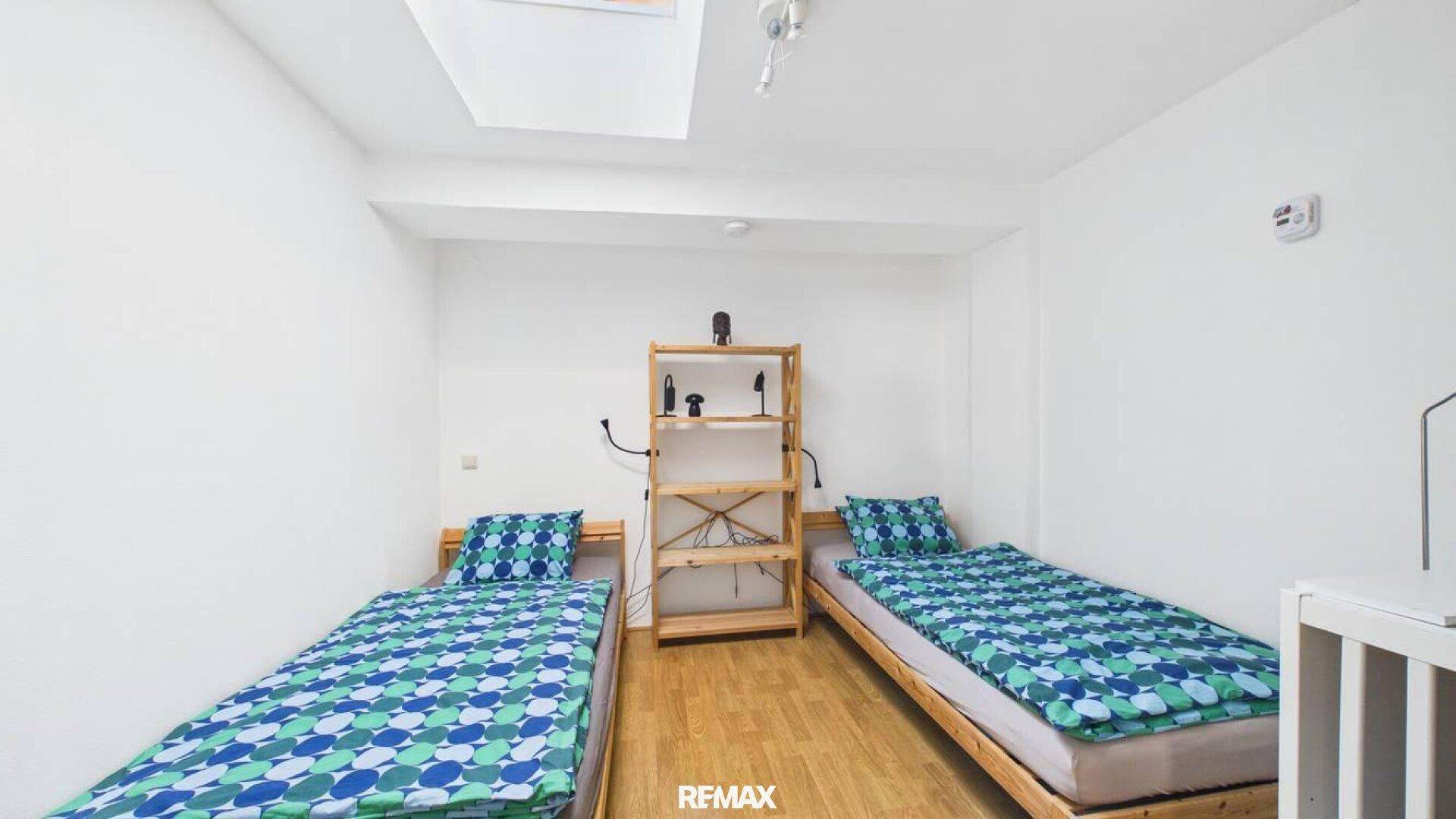 Helles Schlafzimmer mit zwei Einzelbetten, Holzboden und einem Dachfenster.
