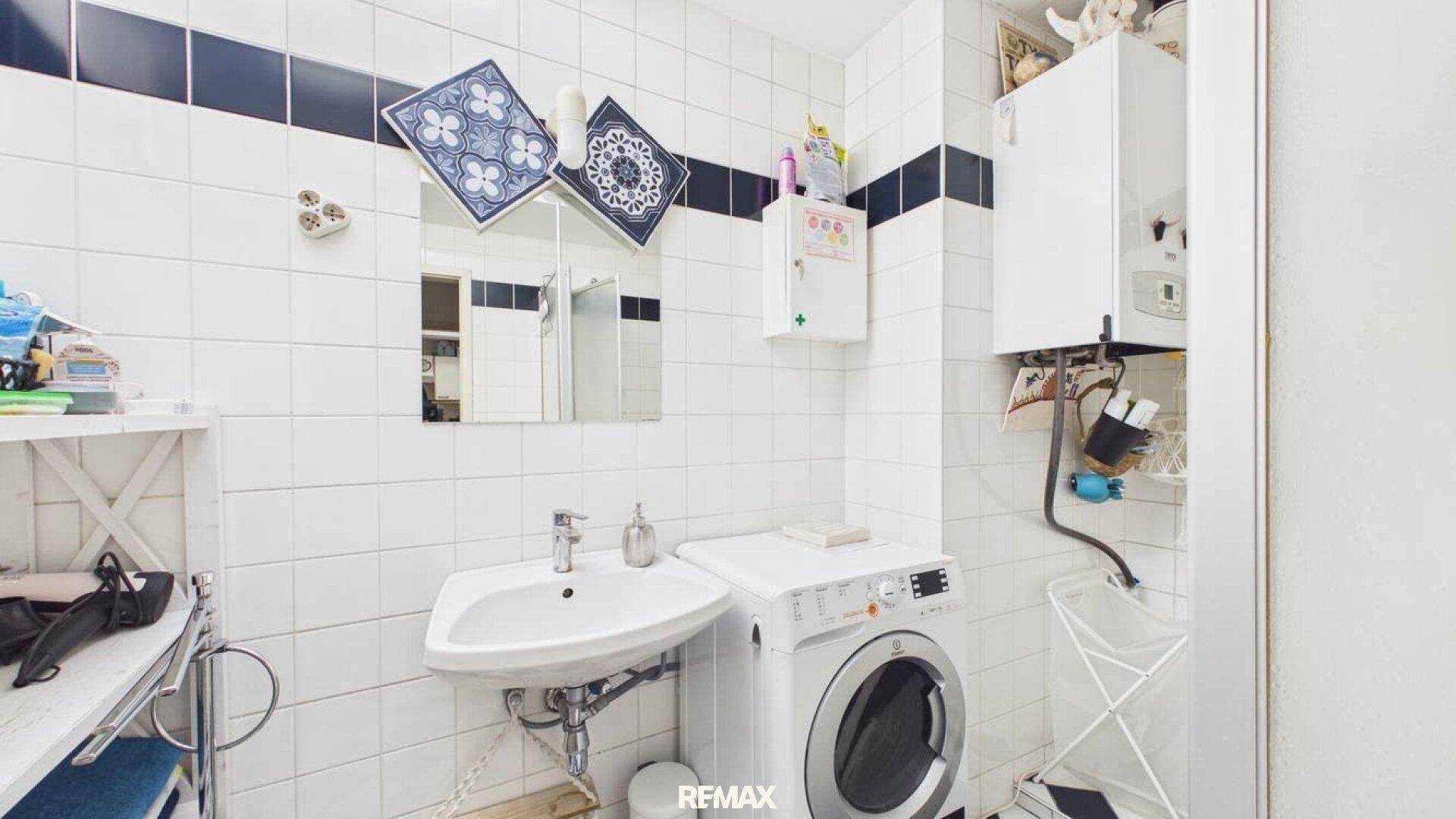 Funktionales Badezimmer mit weißen Fliesen, Waschbecken und Waschmaschine.