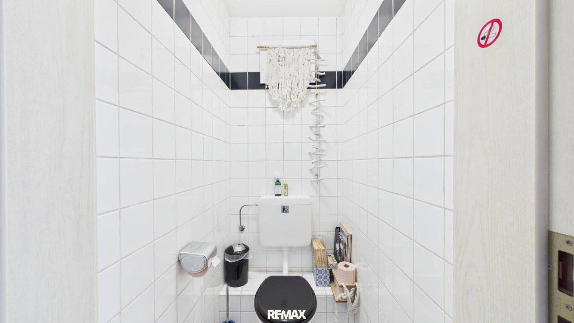 Kleines separates WC mit weißen Fliesen und einer schwarzen Dekorationsleiste.