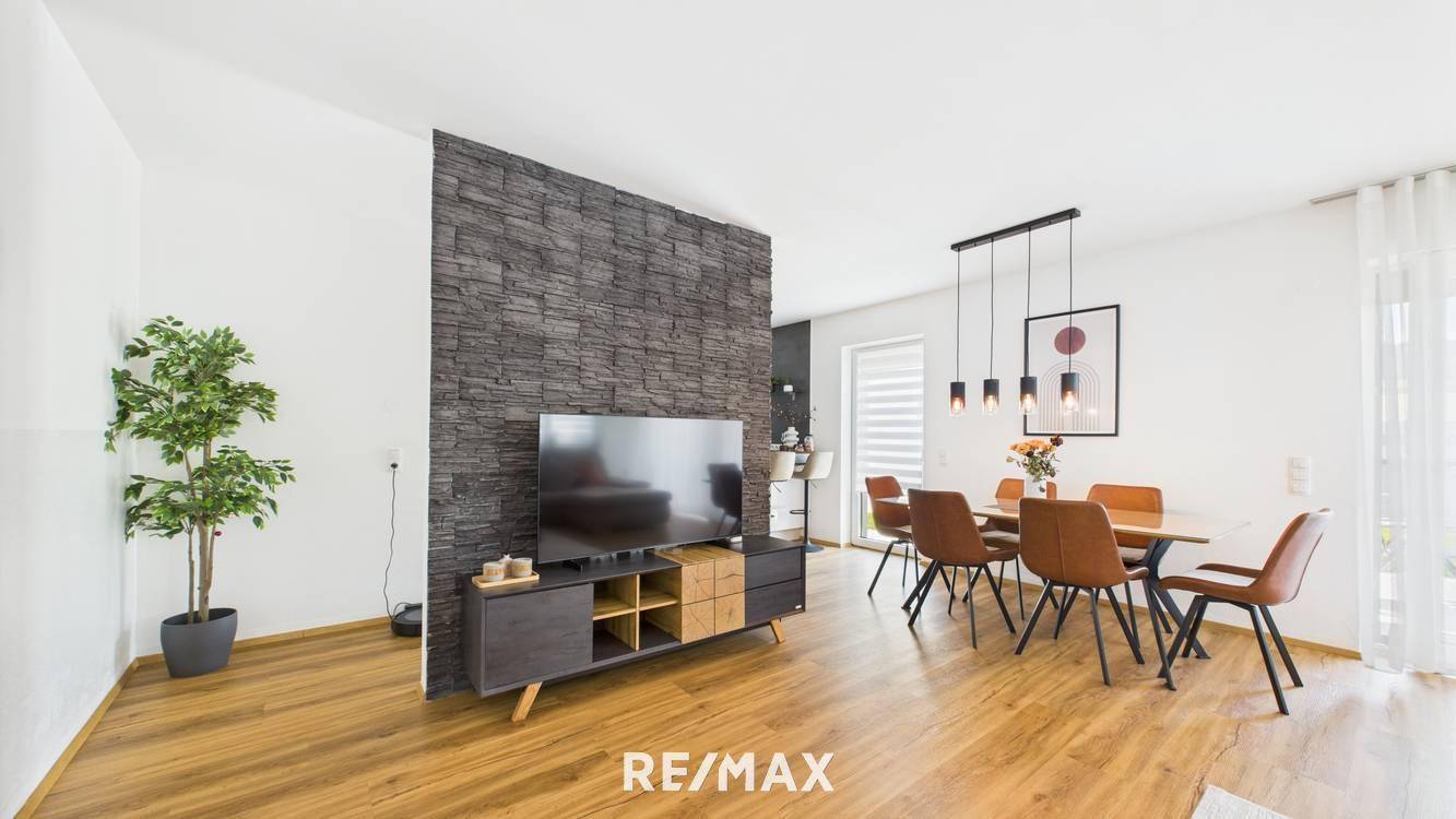 Offener Wohn- und Essbereich mit Holzboden, Steinfurnierwand und modernem Esstisch.