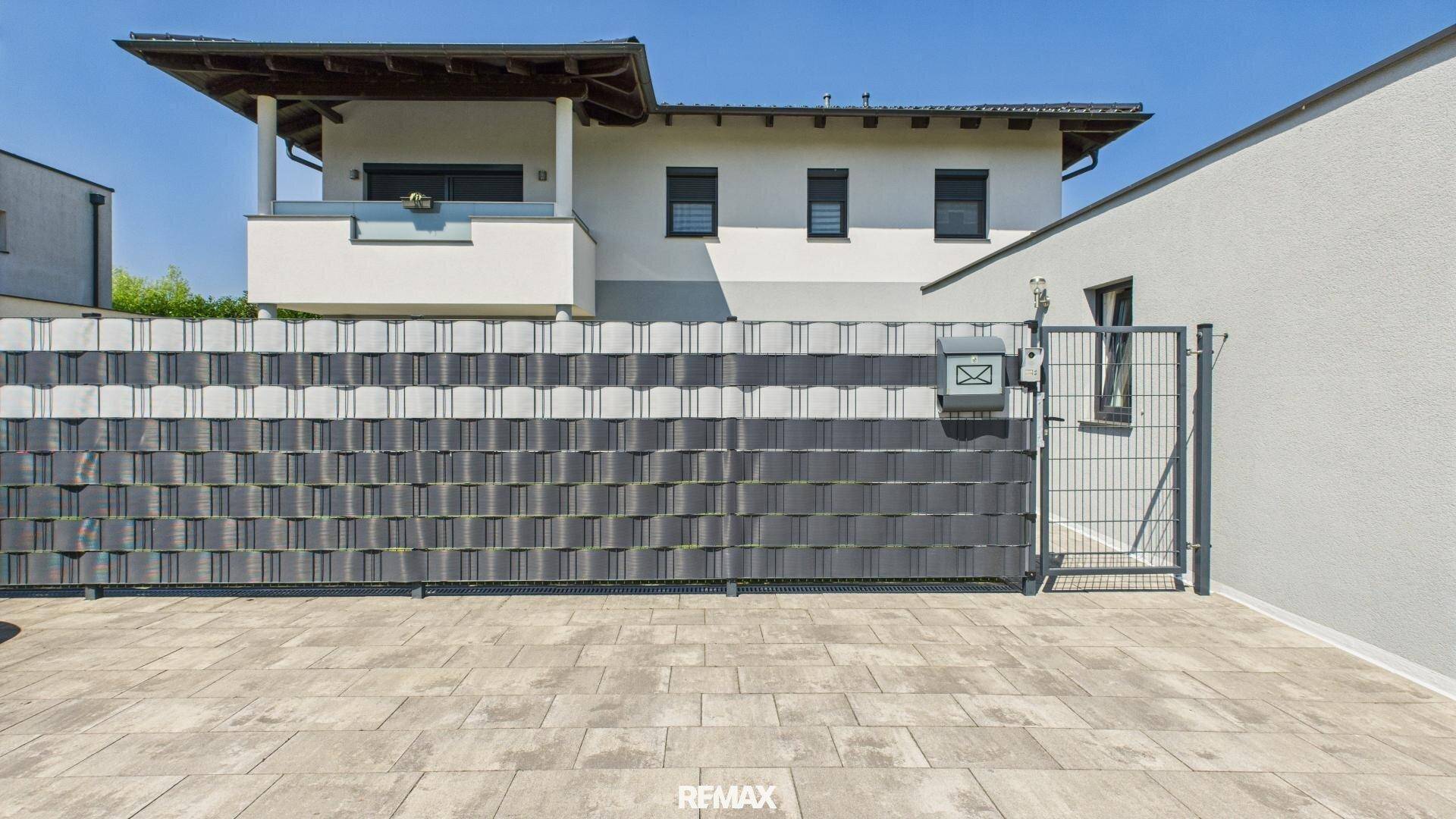 Außenansicht des Hauses mit moderner Zaunanlage und gepflasterter Einfahrt.