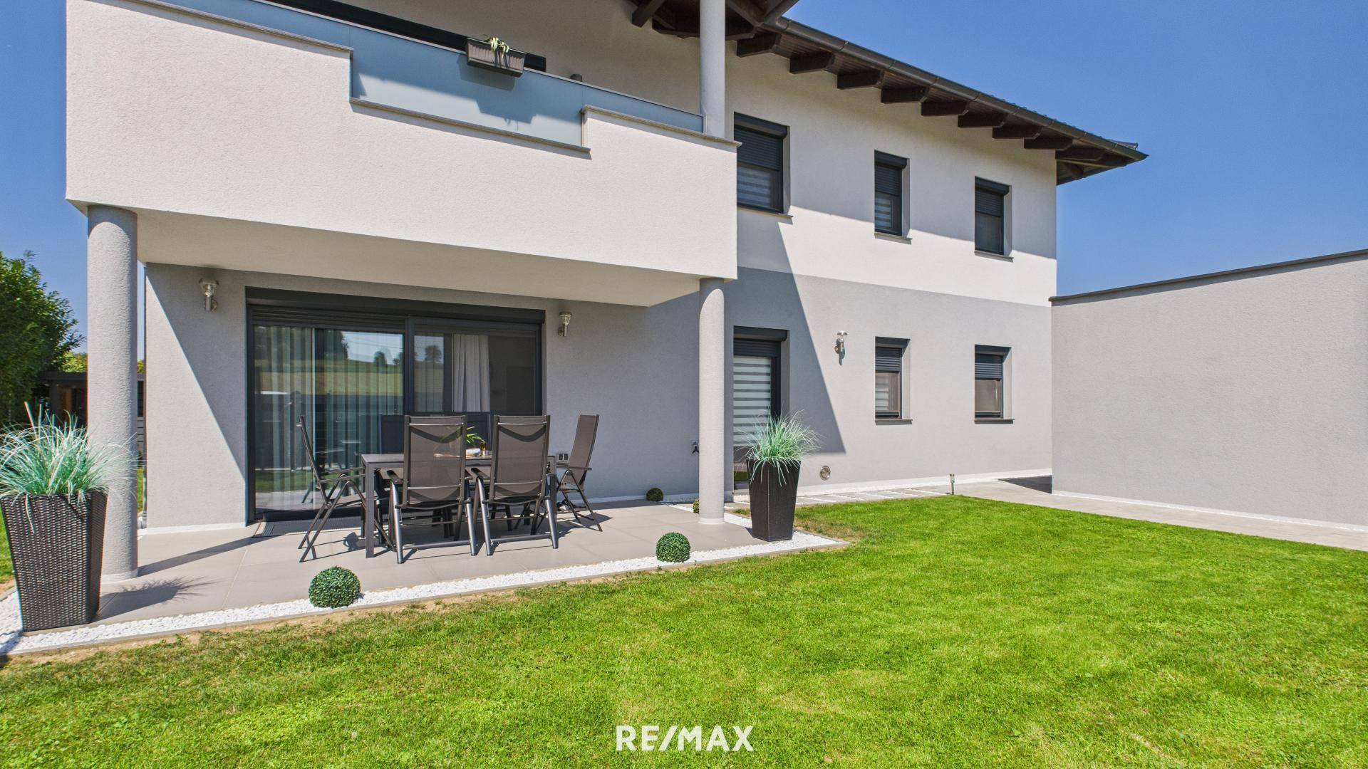 Geräumige Terrasse mit Esstisch und Stühlen, angrenzend an einen grünen Rasenbereich des Hauses.