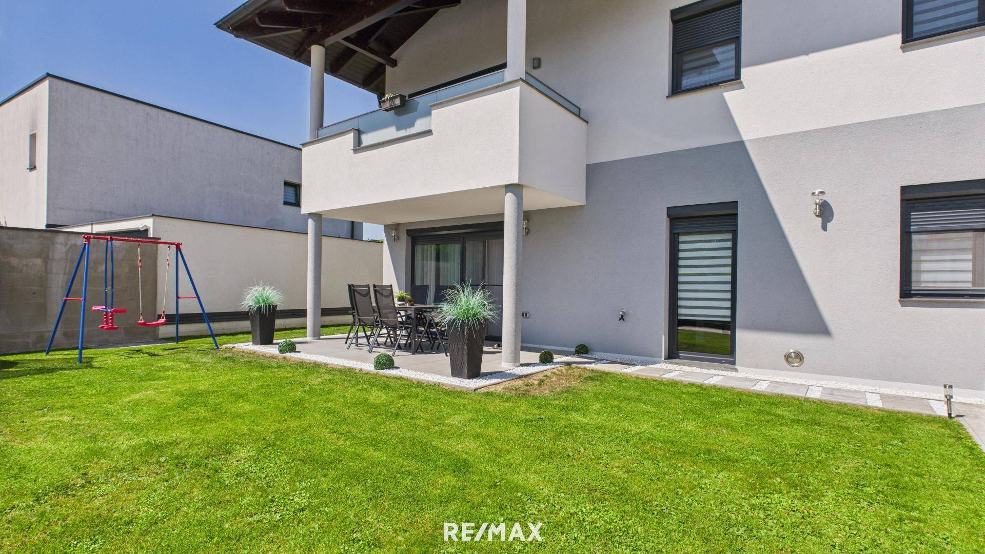 Gepflegter Gartenbereich mit Rasenfläche, Terrasse und Kinderschaukel für Familien.