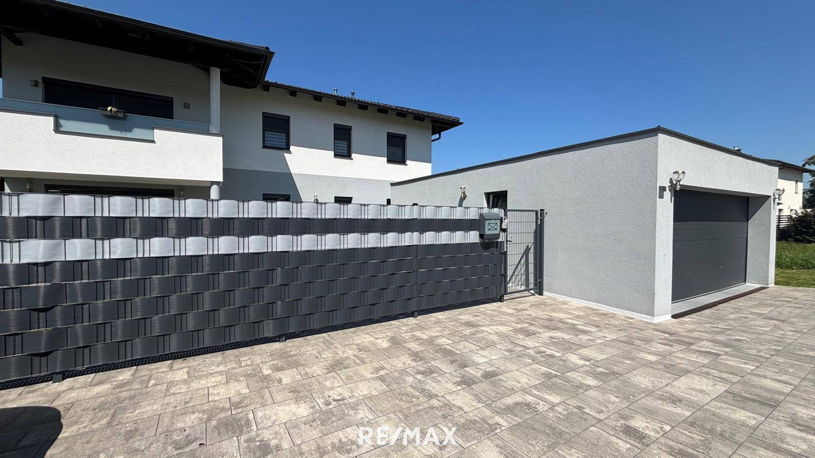 Hausfassade mit Garage, gepflastertem Vorplatz und modernem Sichtschutzzaun.