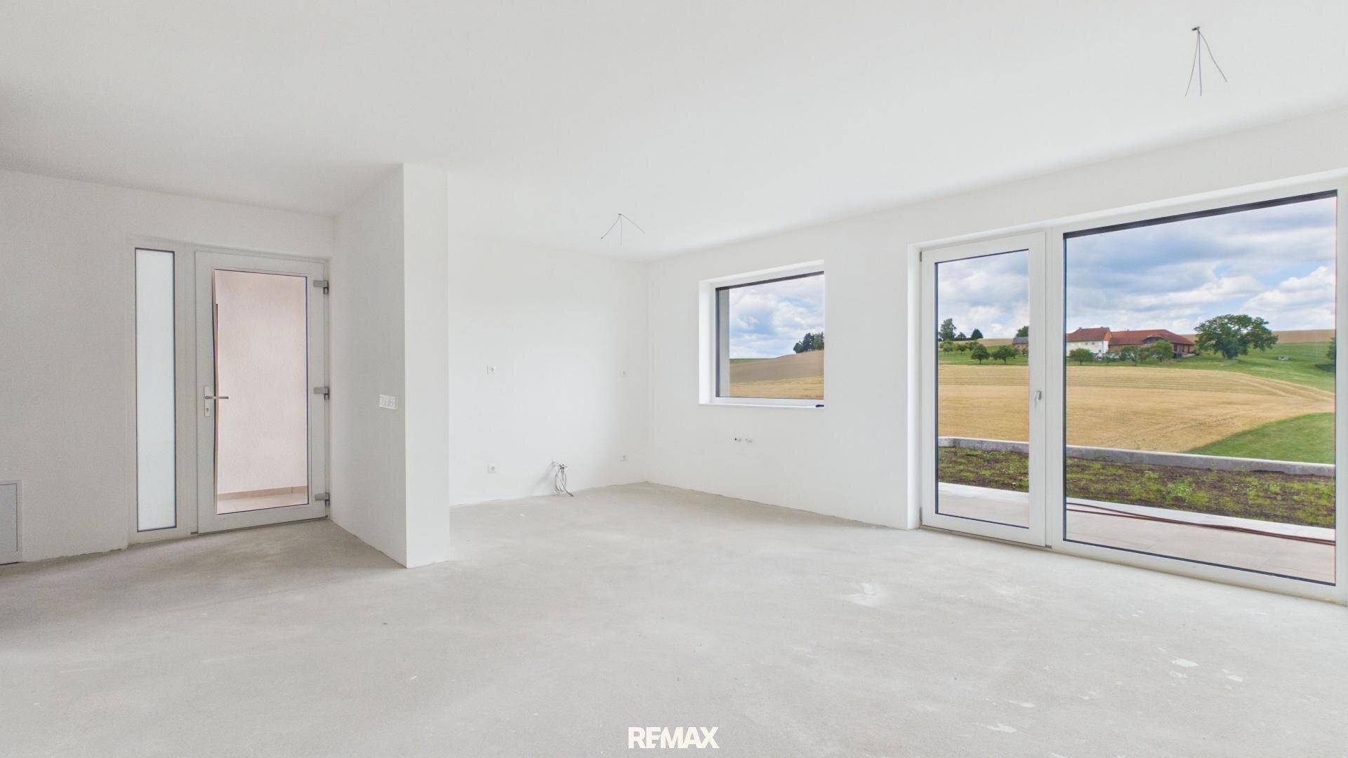 Geräumiger, unfertiger Raum mit großen Fenstern und Zugang nach draußen, bietet Blick auf Felder.