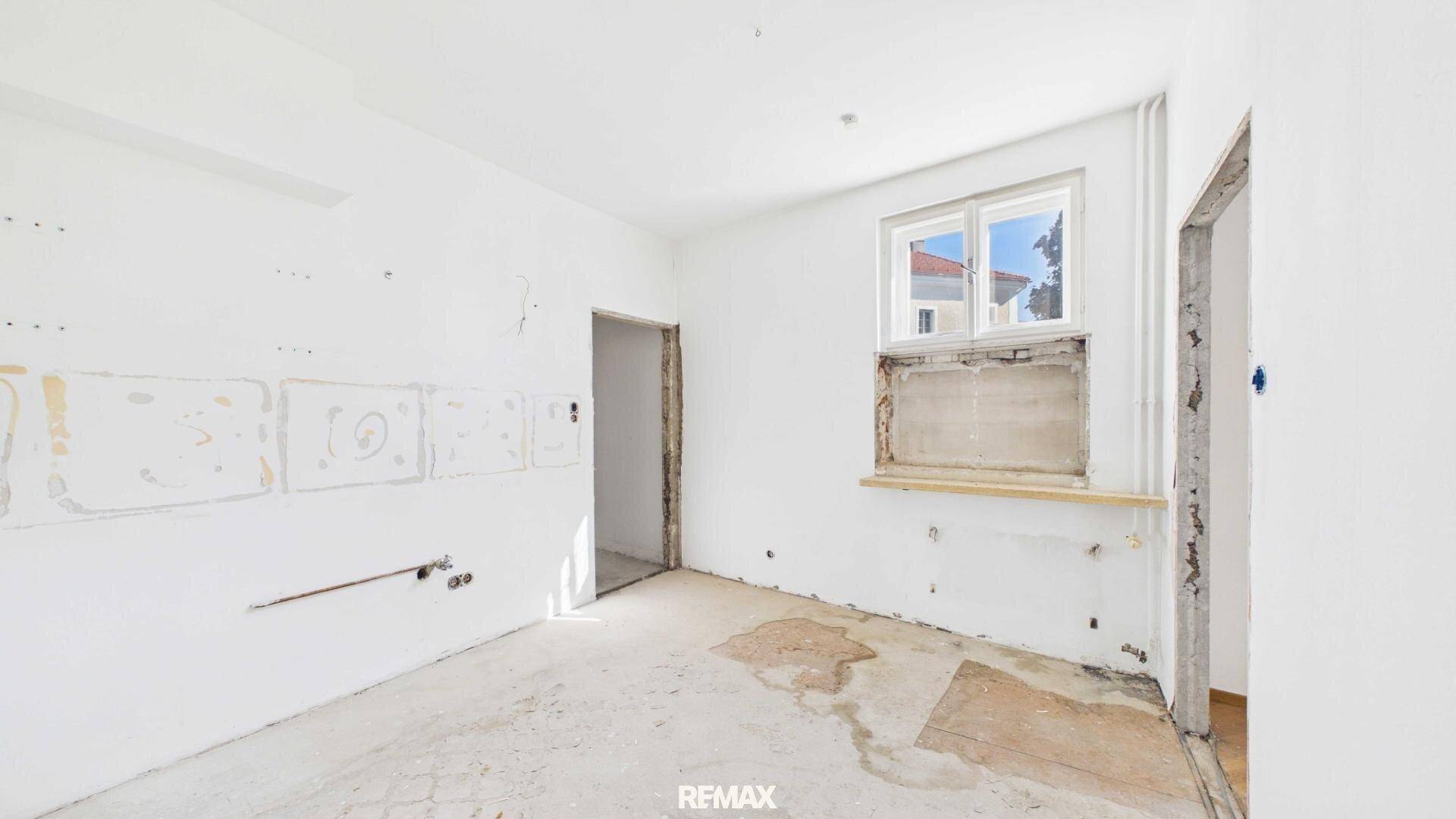 Renovierungsbedürftige Küche mit Fenster und vorbereiteten Anschlüssen.