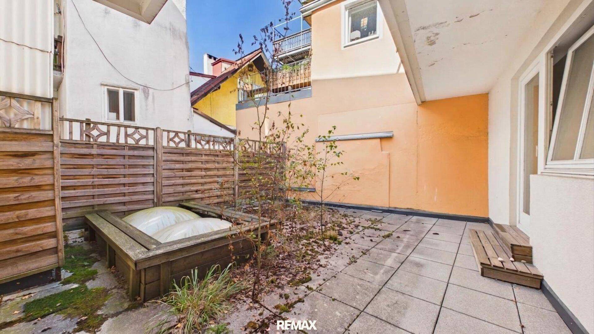 Gepflasterte Terrasse mit Holzzaun, Pflanzen und einem erhöhten Holzbeet im Außenbereich.