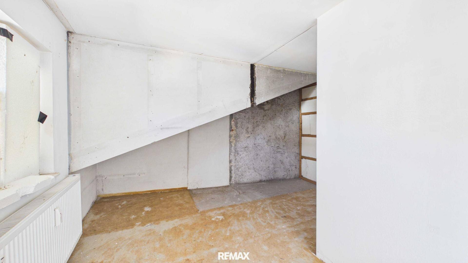 Dachgeschossraum in Renovierung mit schräger Decke und Fenster.