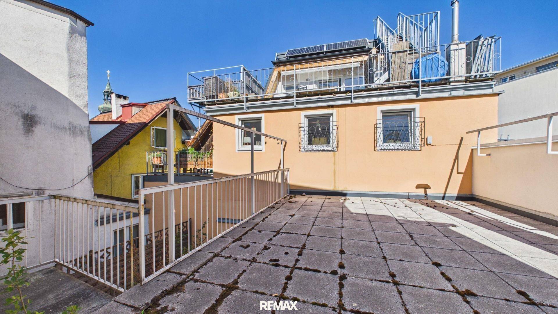 Große Dachterrasse mit Fliesenboden und Blick auf umliegende Gebäude.